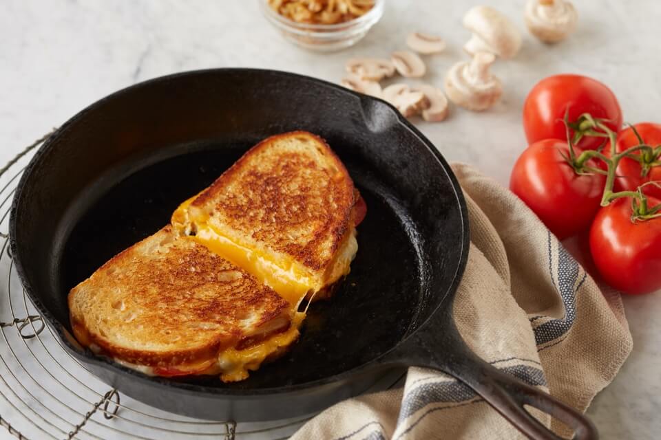 A sandwich toasting-in-a-nonstick-skillet with a lid nearby, showing golden edges forming on the bread in a home kitchen setting