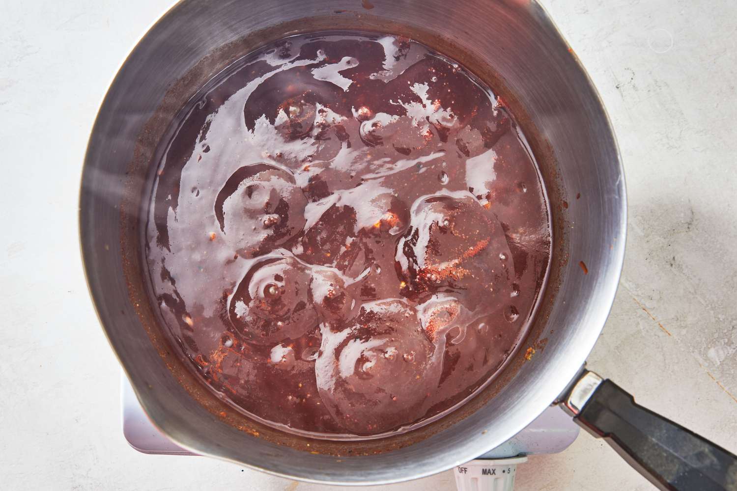 A saucepan of barbecue sauce simmering on a stovetop with a wooden spoon stirring, steam rising in warm kitchen light