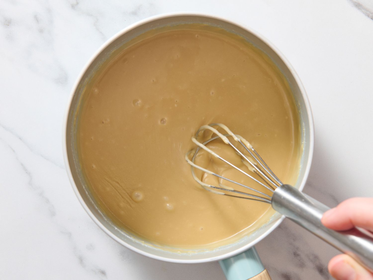 A saucepan of bubbling caramel icing being stirred with a wooden spoon on a stovetop, steam rising in warm kitchen light