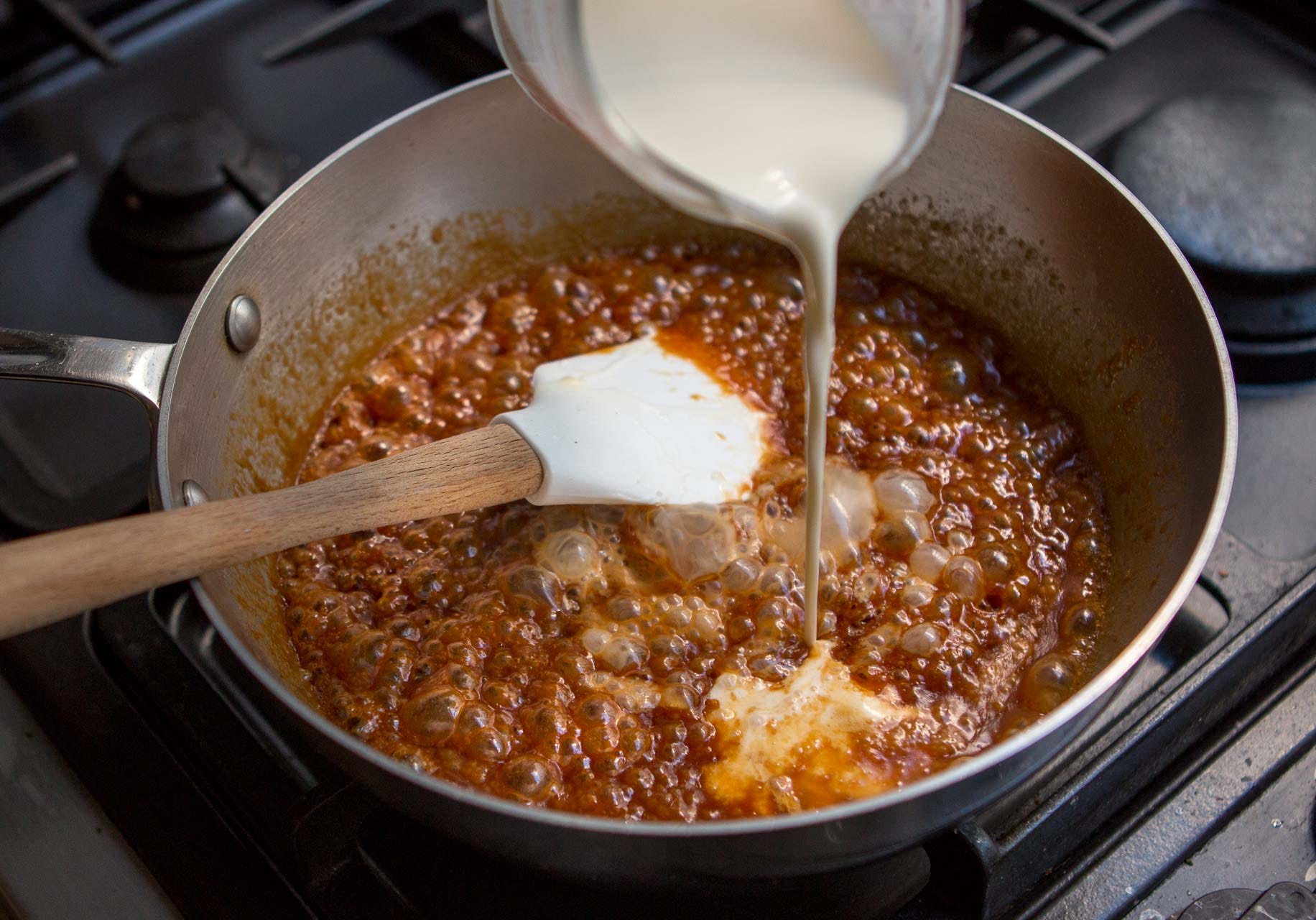 A saucepan of bubbling caramel sauce being whisked on a stovetop with warm kitchen lighting