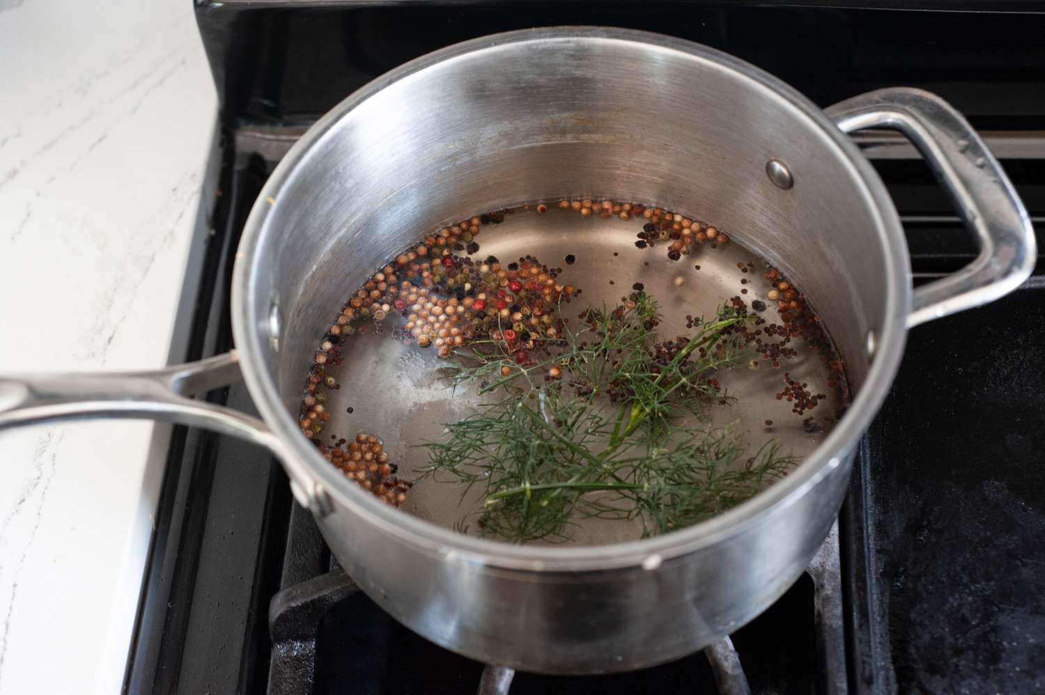 A saucepan of clear vinegar brine simmering with whole spices floating on the surface