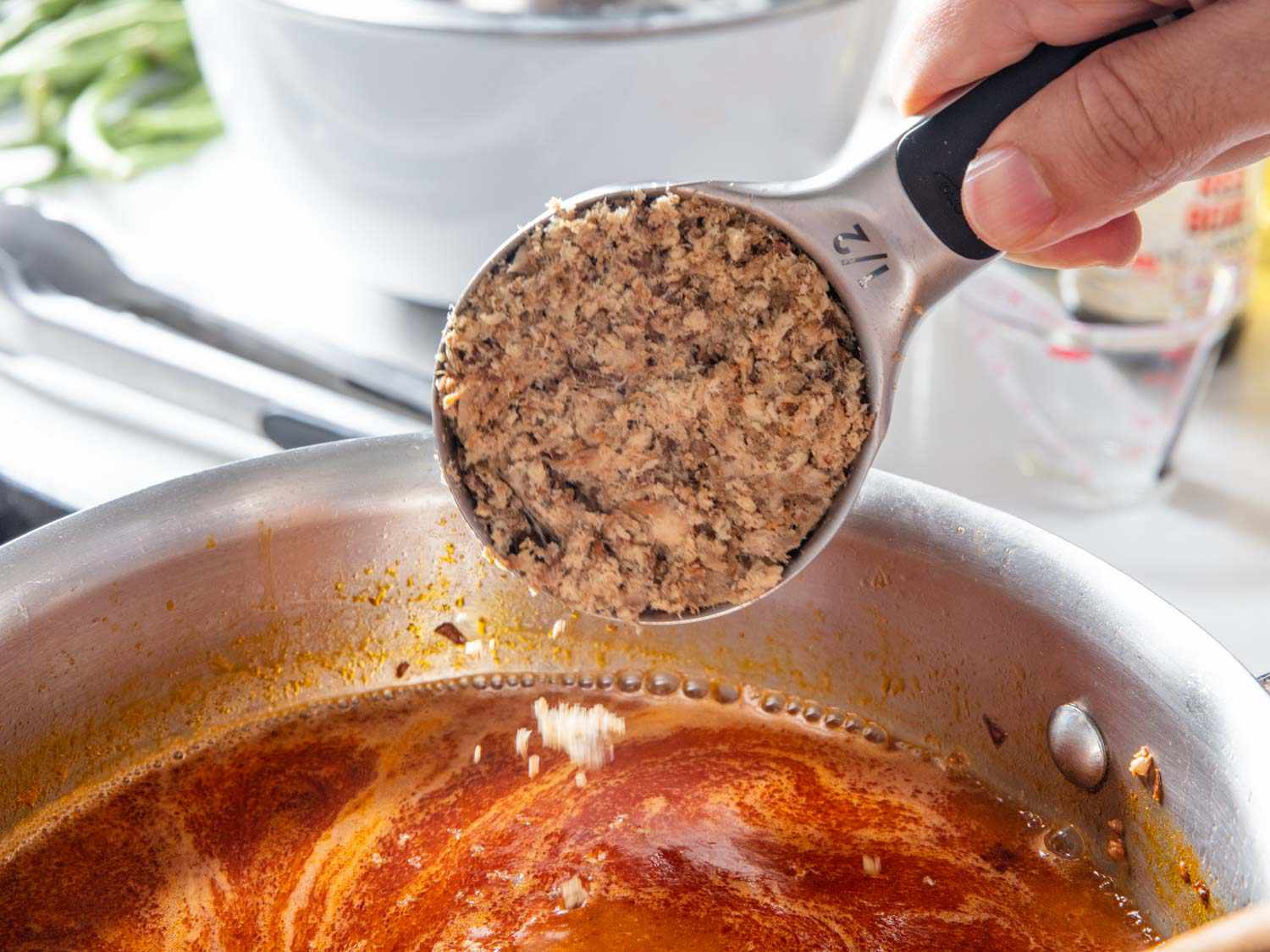 A saucepan of orange-gold palabok sauce being whisked smooth on a stovetop, with garlic and annatto visible