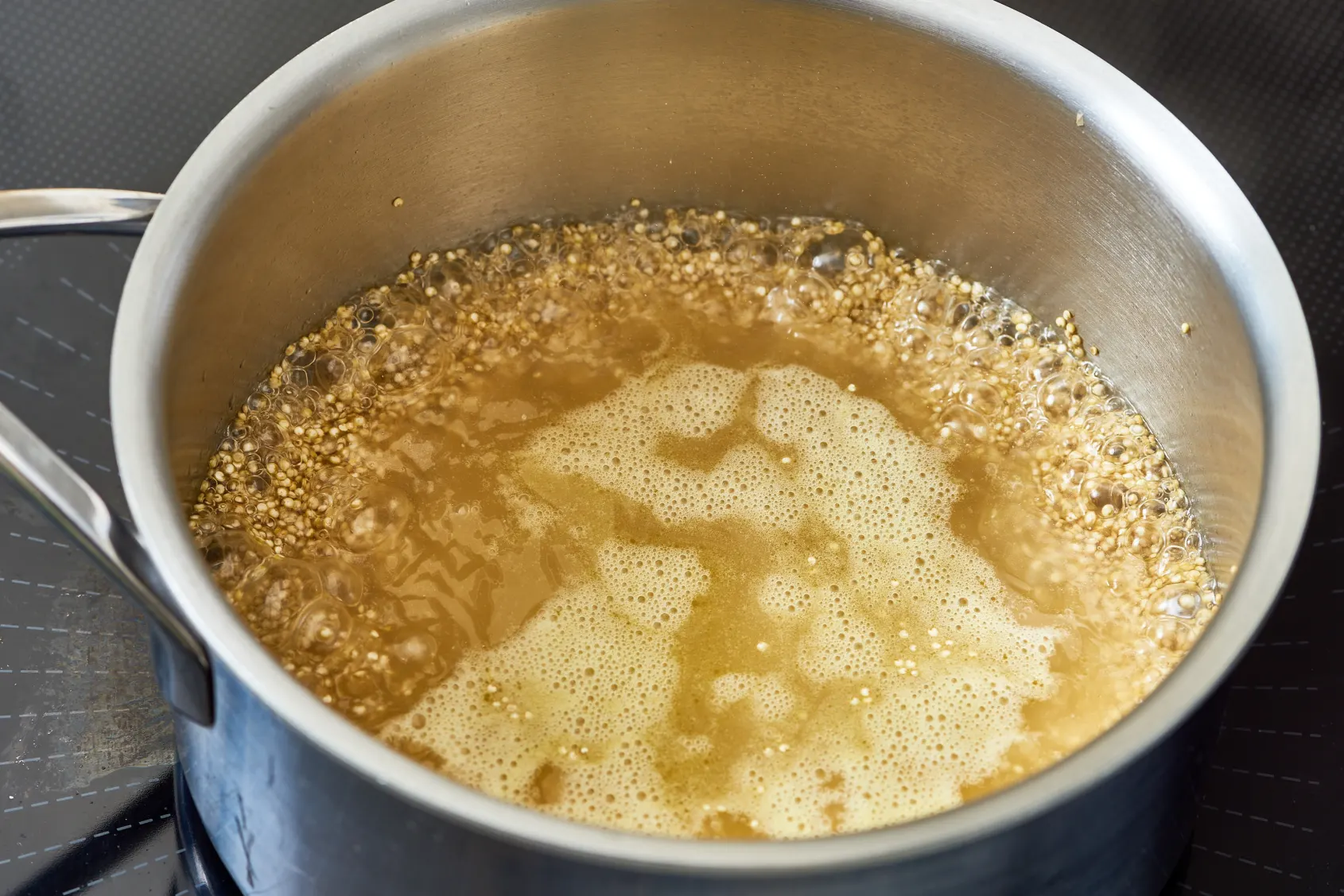 A saucepan of quinoa simmering on a stovetop with the lid slightly ajar and gentle steam rising