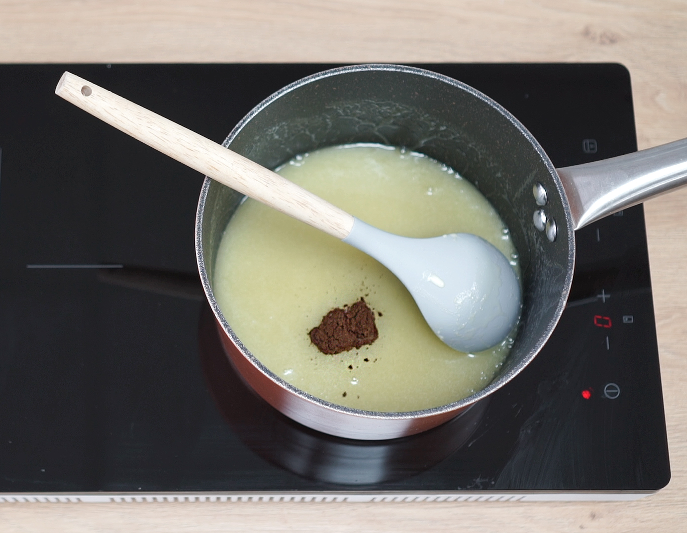 A saucepan of warm cream and milk being whisked as espresso powder dissolves, creating a light brown coffee base