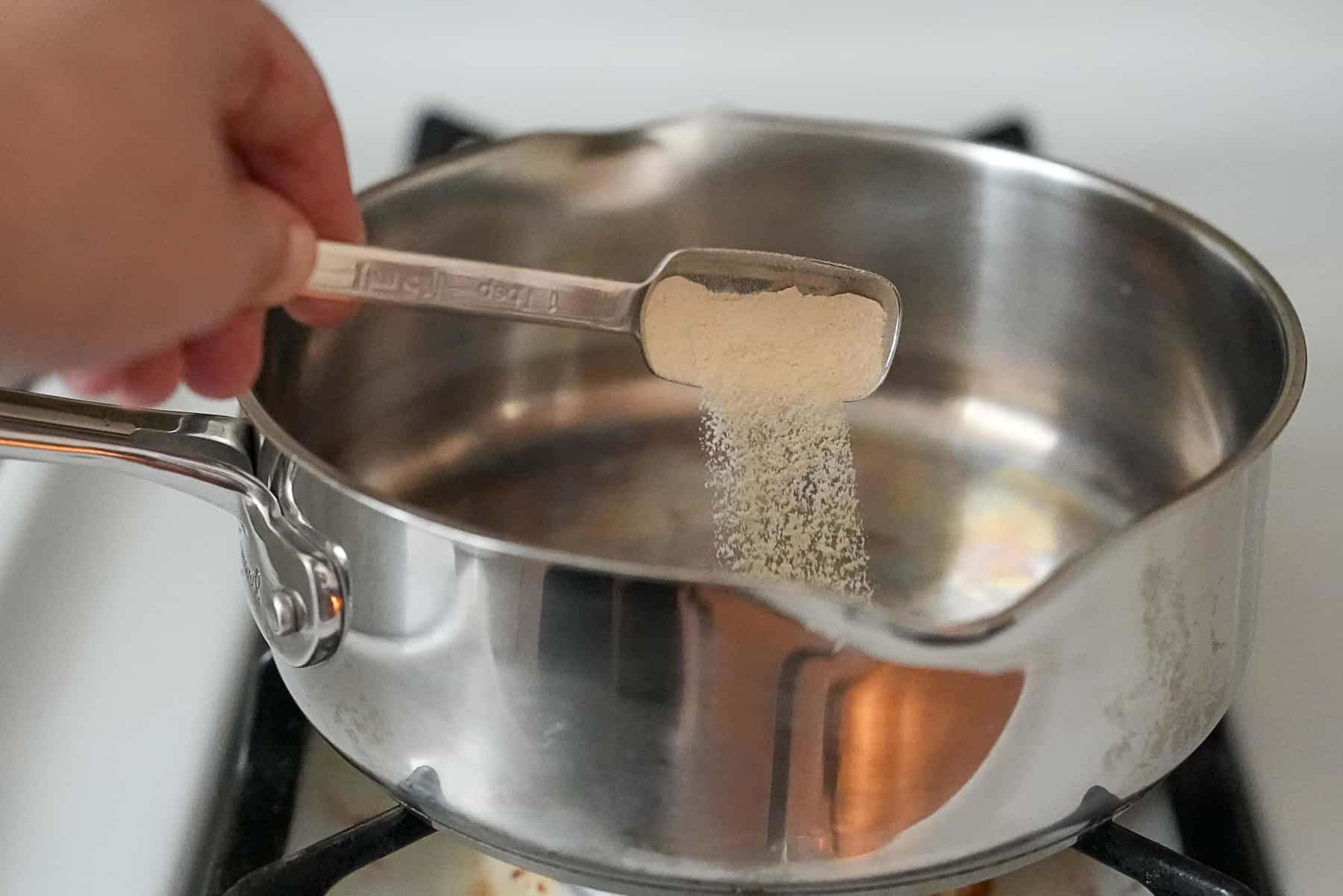 A saucepan on the stove with green gelatin being whisked smooth, steam rising lightly in a home kitchen