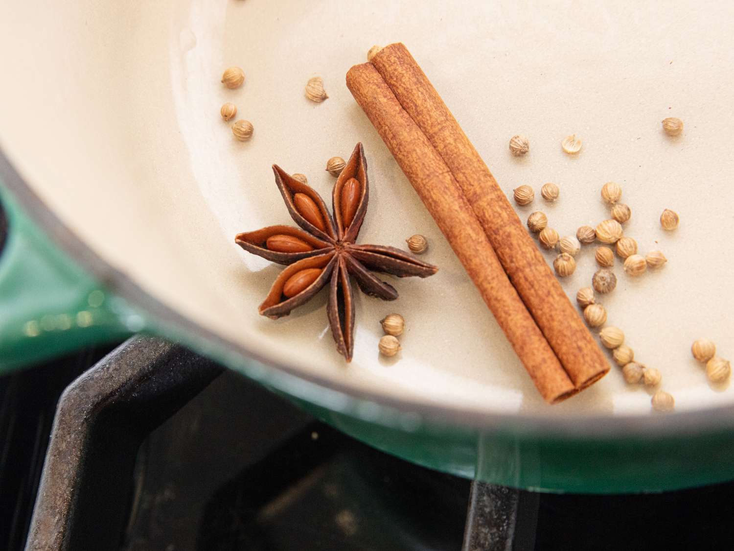 A saucepan on the stove with red wine, orange slices, cinnamon sticks, cloves, and star anise before heating