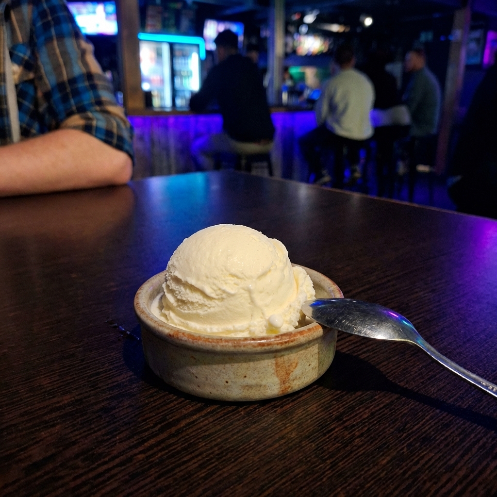 A scoop of vanilla ice cream in a small ceramic dish with a spoon beside it
