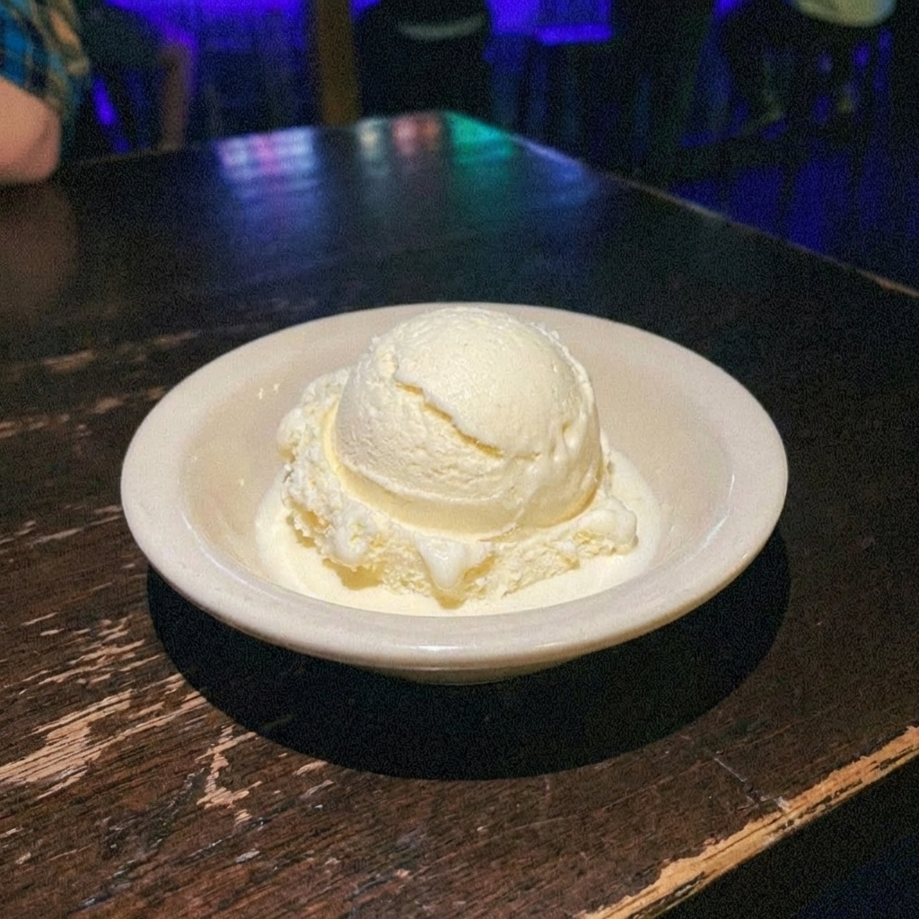 A scoop of vanilla ice cream melting slightly in a small bowl