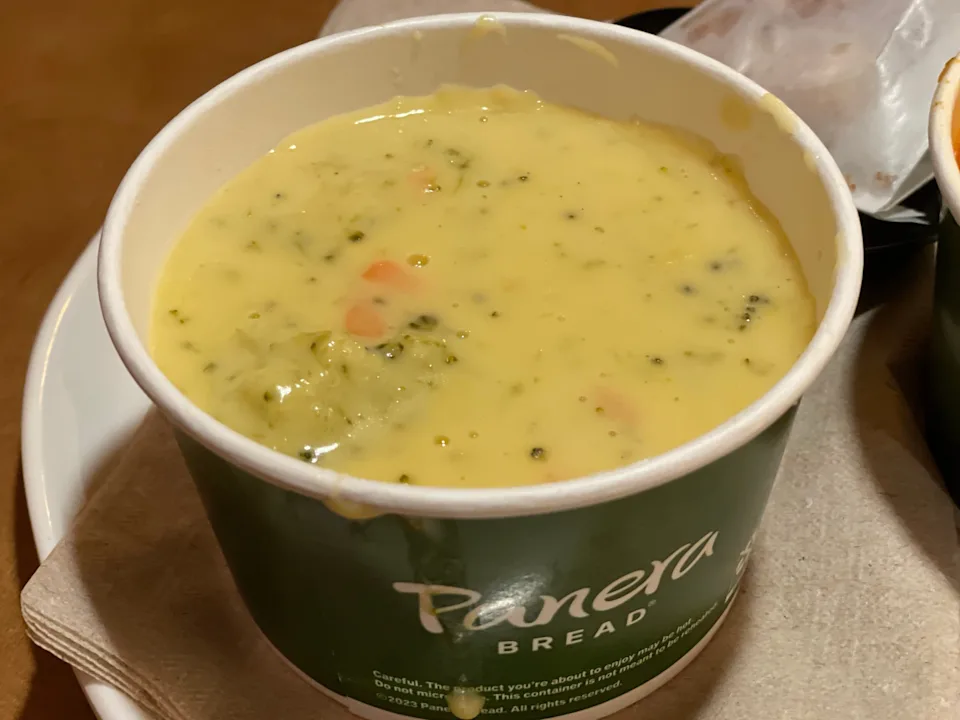 A sealed glass container filled with broccoli cheddar soup on a refrigerator shelf in warm kitchen light