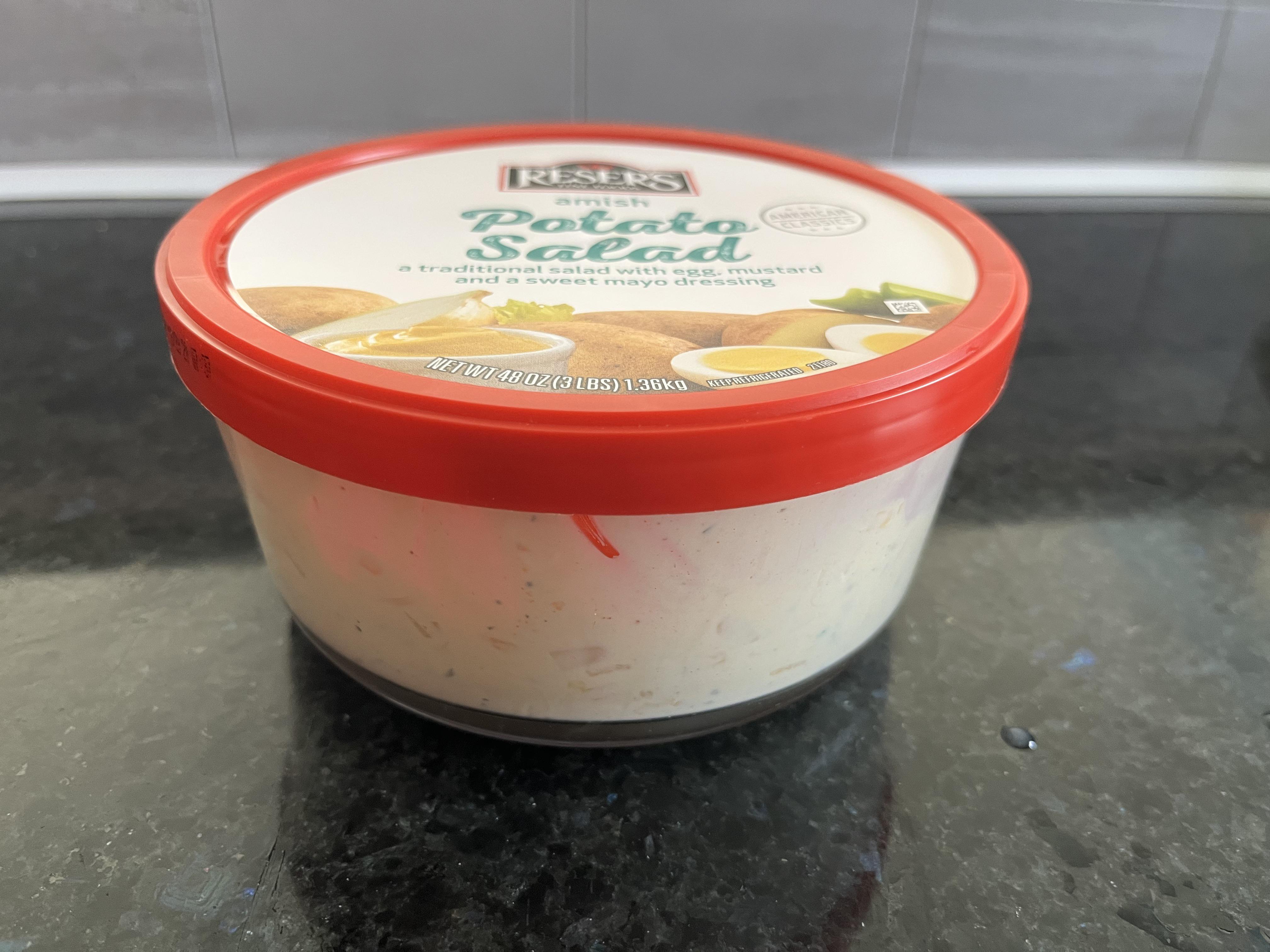 A sealed glass container of potato salad on a refrigerator shelf next to other meal prep containers