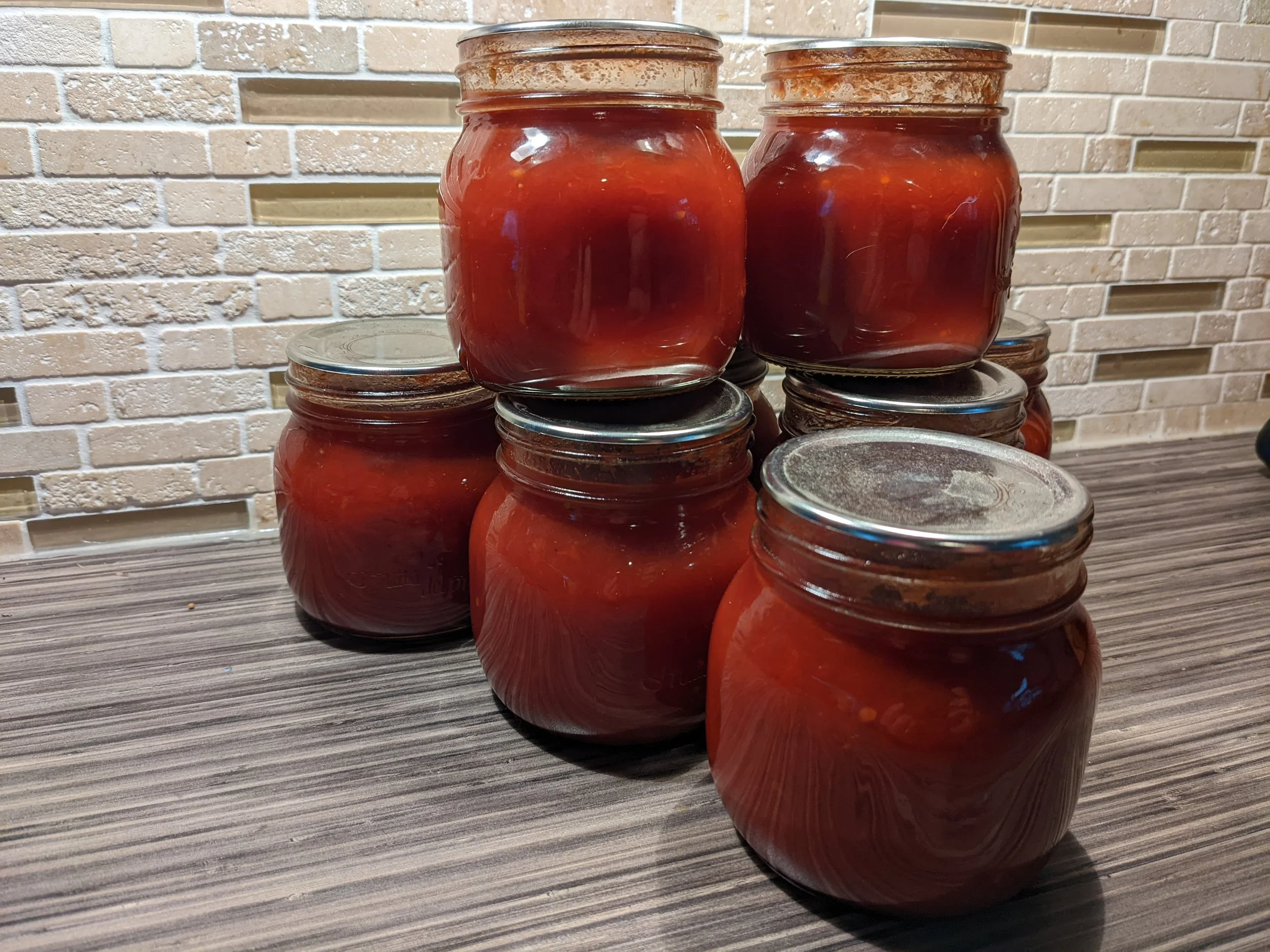 A sealed glass jar of homemade ketchup sitting on a refrigerator shelf next to other condiments