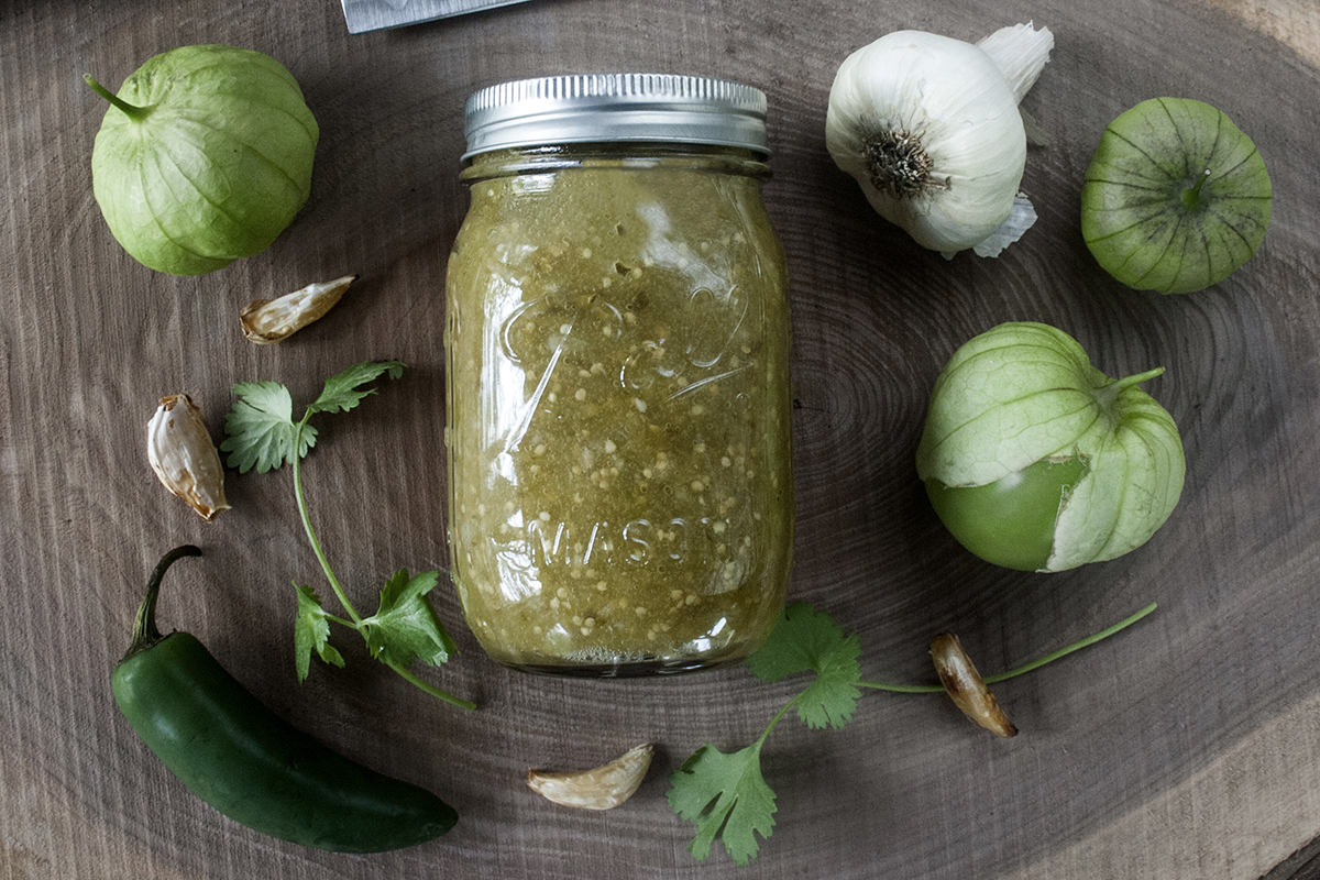 A sealed mason jar filled with green tomatillo salsa sitting on a refrigerator shelf