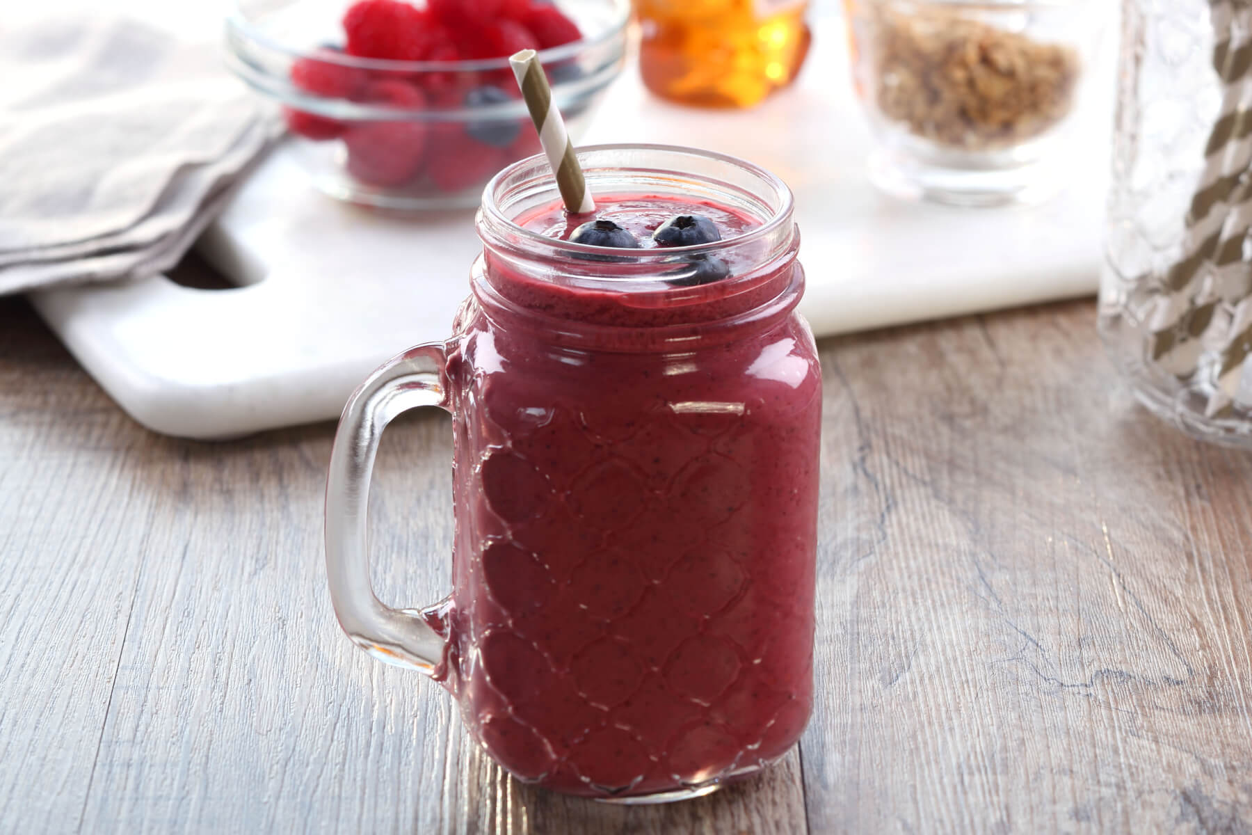 A sealed mason jar of berry fruit shake sitting on a refrigerator shelf with condensation on the glass