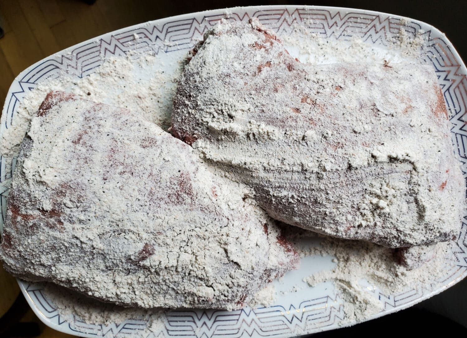 A seasoned chuck roast on a wooden cutting board with salt, pepper, and a light dusting of flour visible on the surface