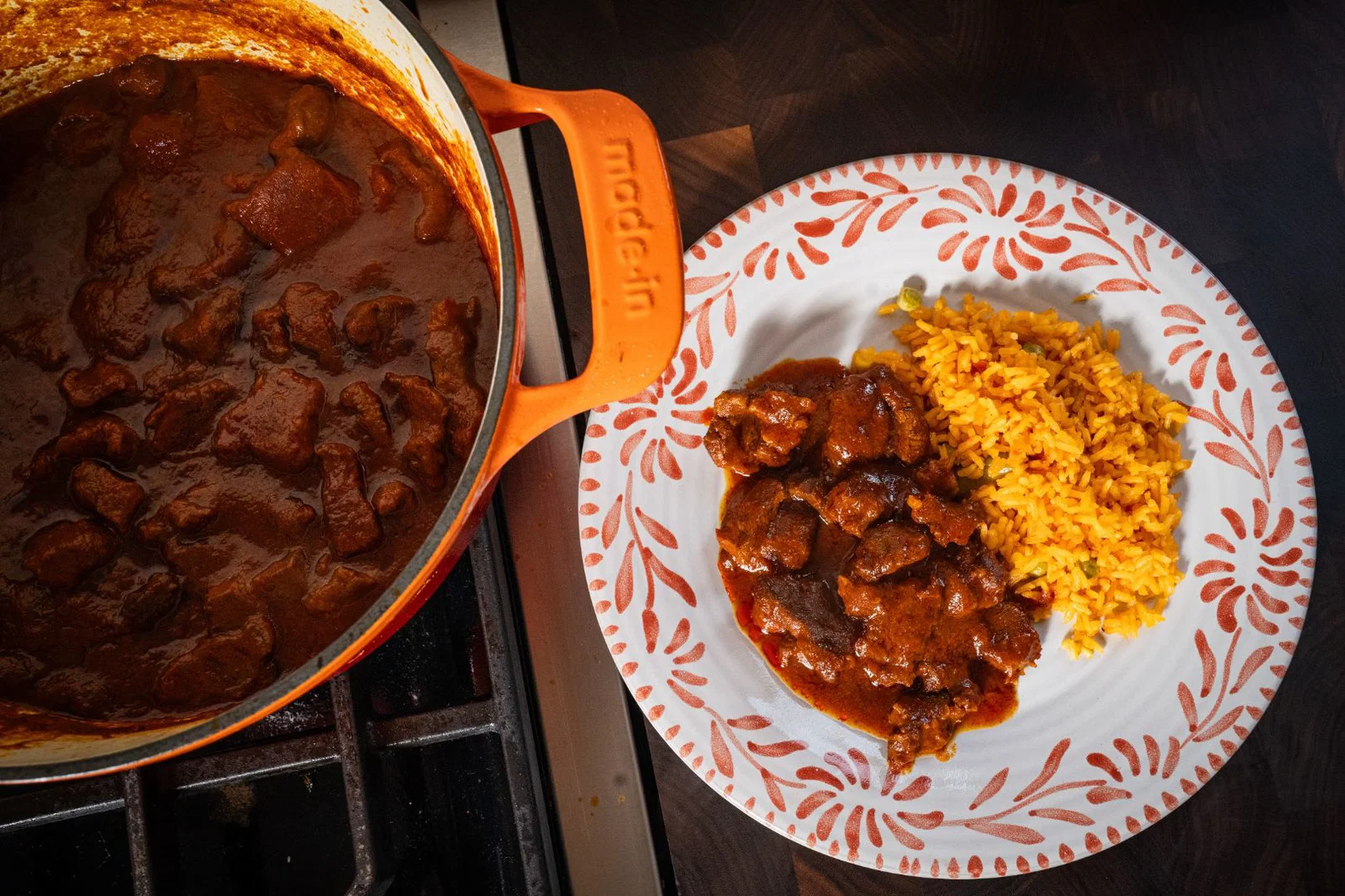 A serving of chili colorado on a plate with Mexican rice and warm corn tortillas on the side, set on a kitchen table with soft window light