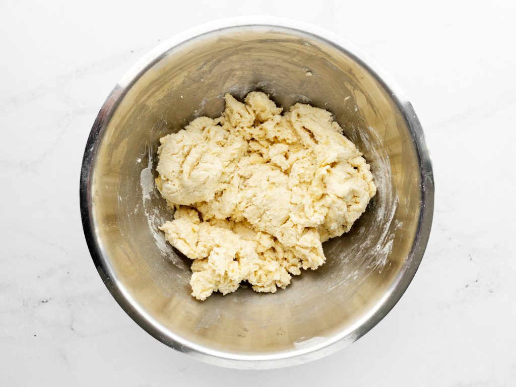 A shaggy flatbread dough being mixed in a large bowl with a wooden spoon, with a little flour still visible around the edges