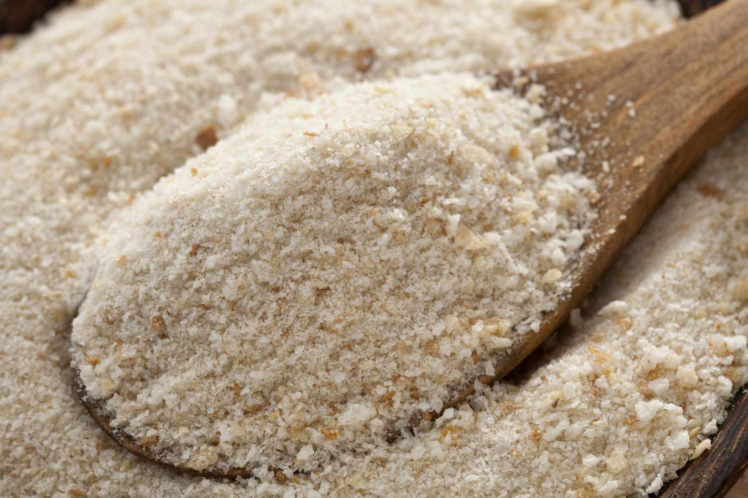 A shallow bowl filled with fine dry breadcrumbs on a kitchen counter next to a parchment lined baking sheet