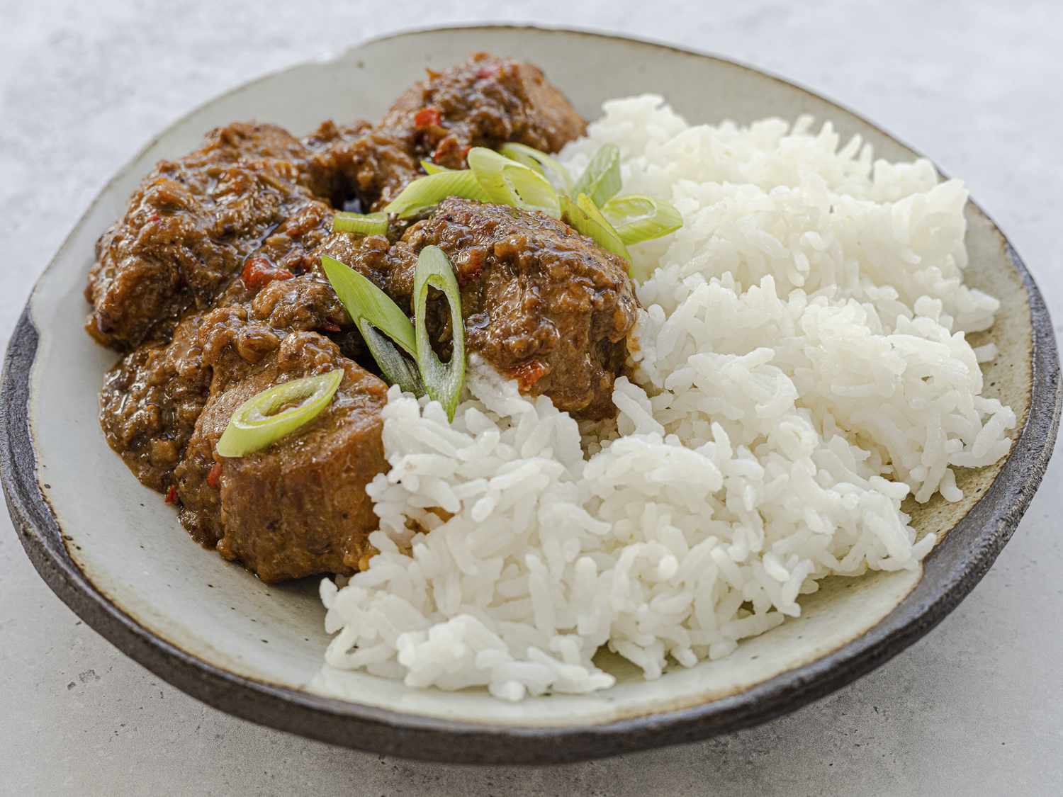 A shallow bowl of Bicol Express with tender pork pieces in a creamy coconut sauce, flecked with red and green chiles, served with steamed white rice on a simple wooden table