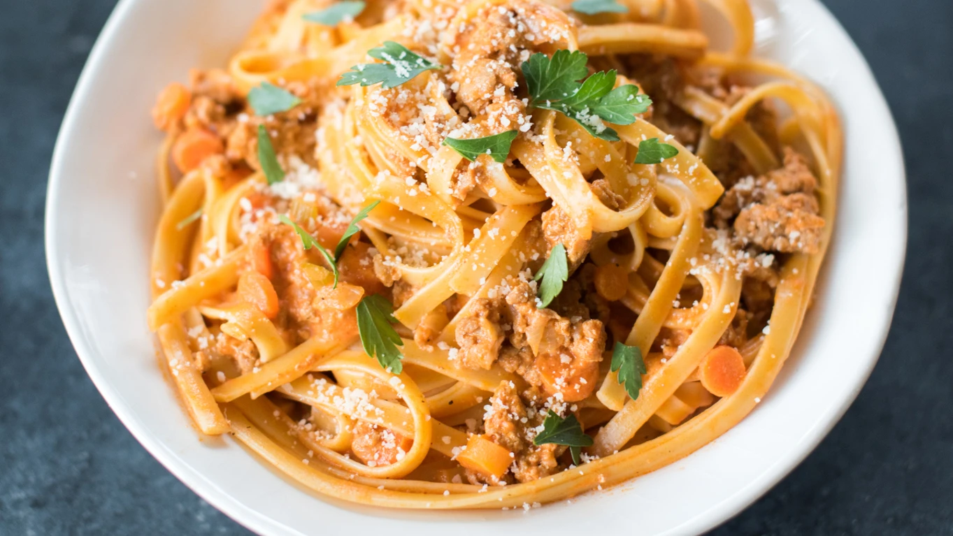 A shallow bowl of creamy ground turkey pasta in a tomato cream sauce with spinach and grated Parmesan on top, sitting on a wooden table with a fork beside it