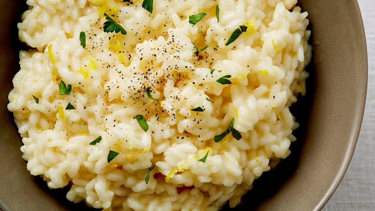 A shallow bowl of creamy lemon Parmesan risotto with green peas and black pepper on a linen napkin beside a spoon on a wooden table