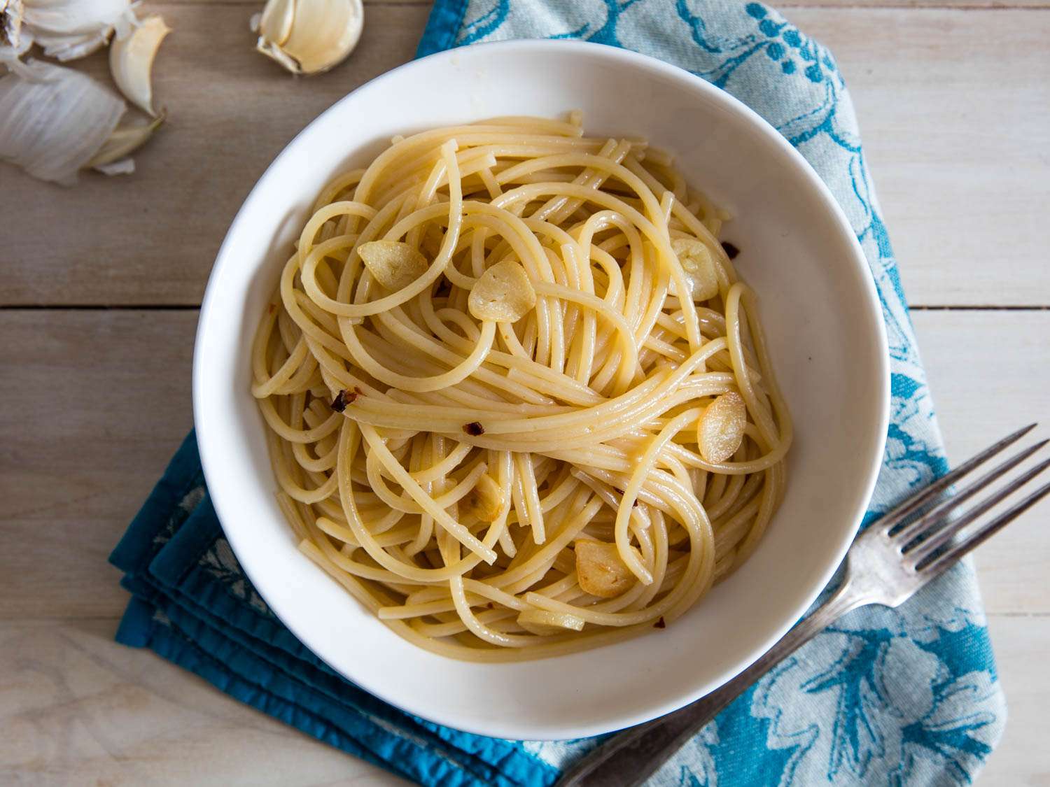 A shallow bowl of spaghetti tossed in glossy garlic olive oil sauce and topped with a dollop of lemon aioli, parsley, and red pepper flakes on a wooden table