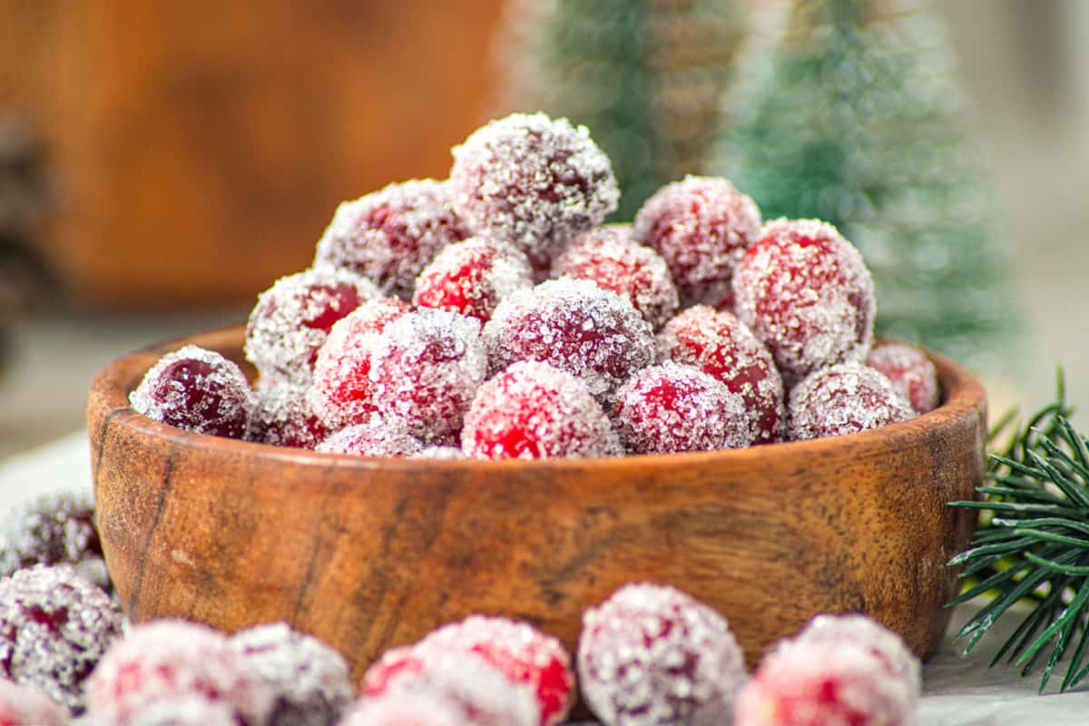 A shallow bowl of sugar-coated candied cranberries sparkling under warm kitchen light on a neutral stone countertop