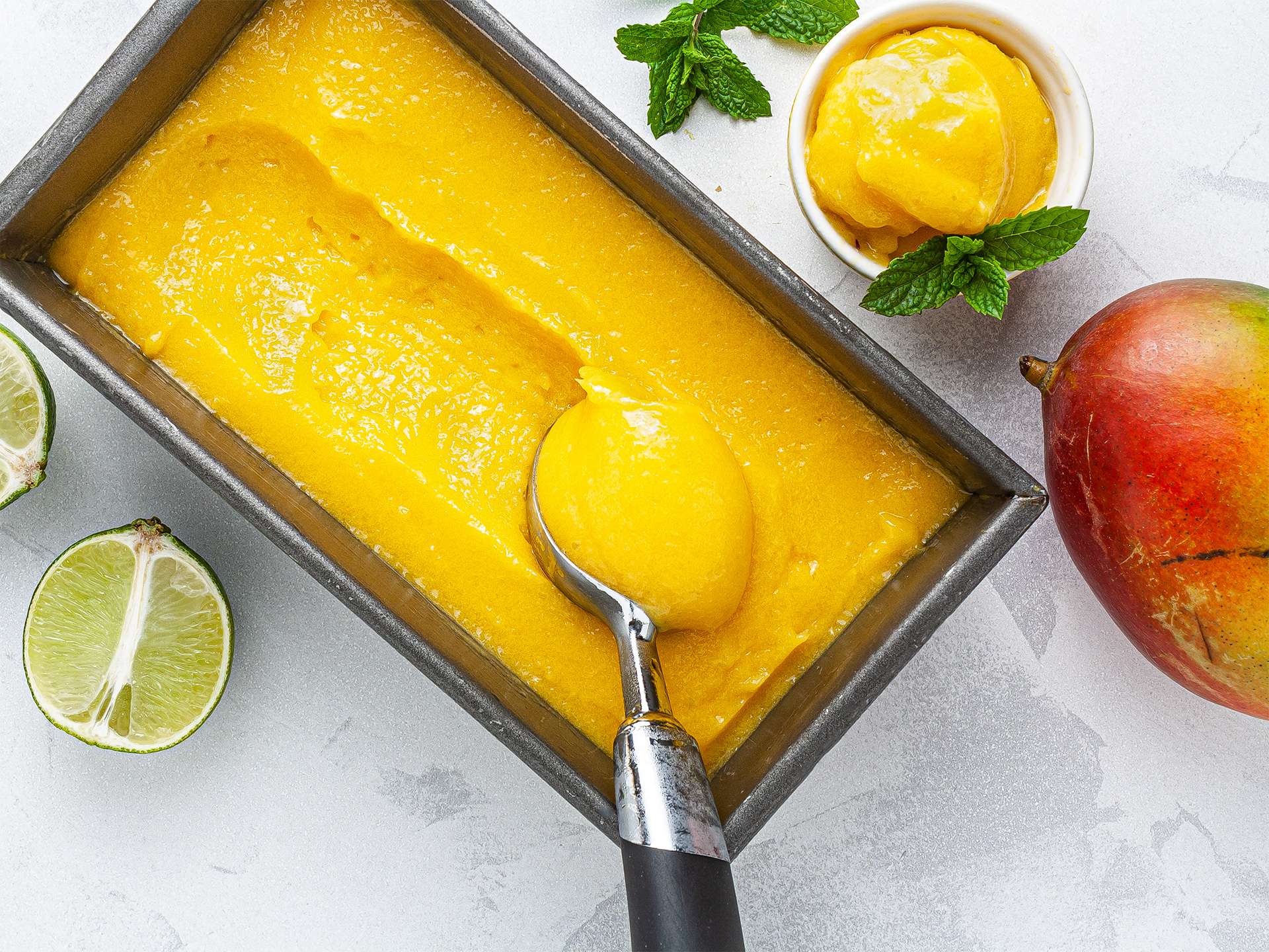 A shallow freezer container filled with mango sorbet with parchment pressed on top