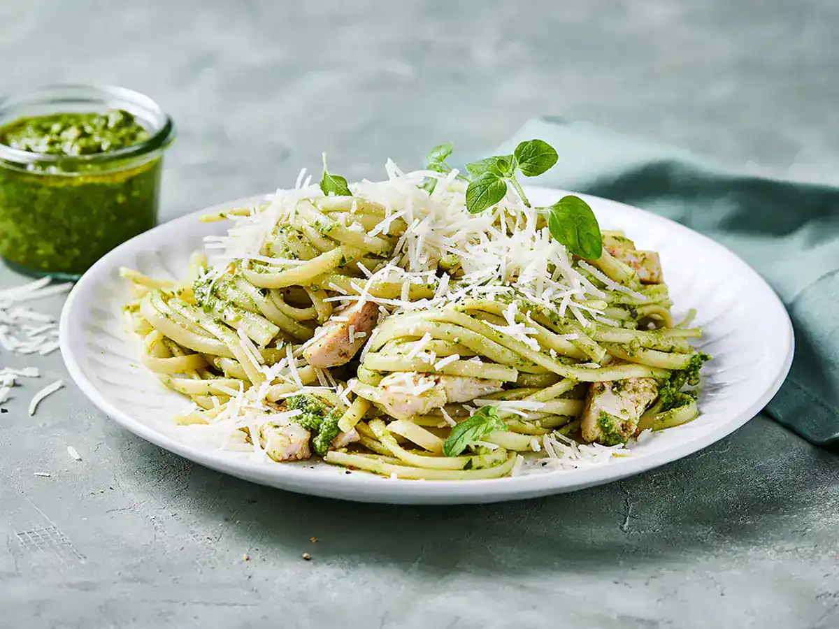 A shallow skillet filled with creamy chicken pesto pasta and wilted spinach, finished with grated Parmesan on a warm kitchen counter
