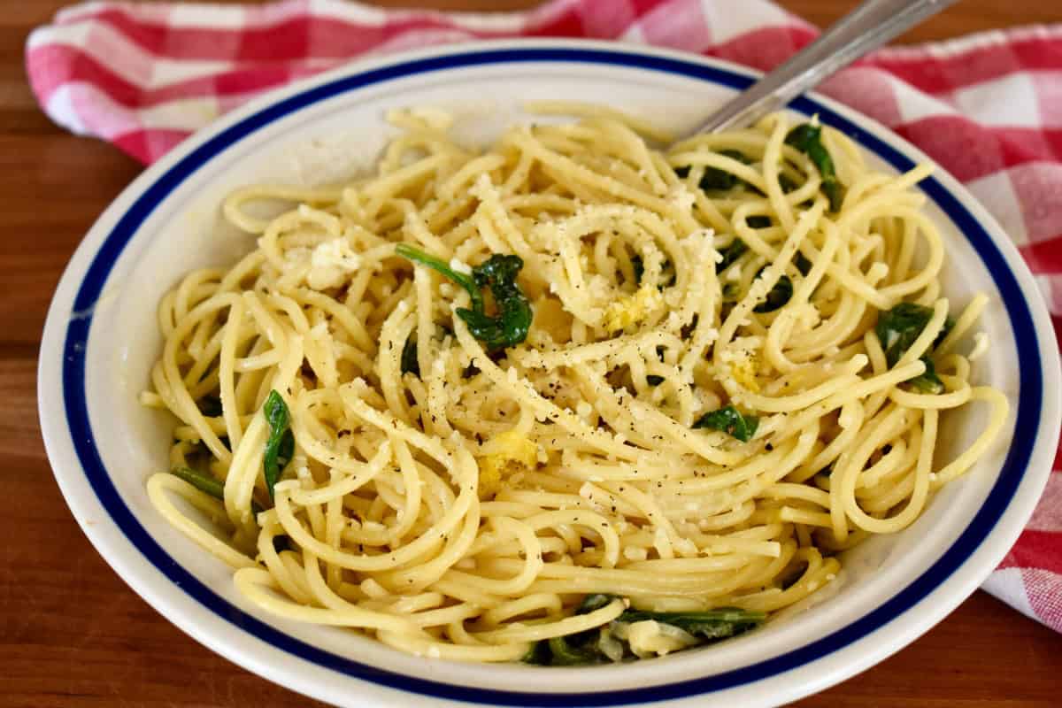 A shallow skillet of creamy lemon mascarpone pasta being tossed with tongs, topped with grated Parmesan and black pepper, on a warm-lit home kitchen stove