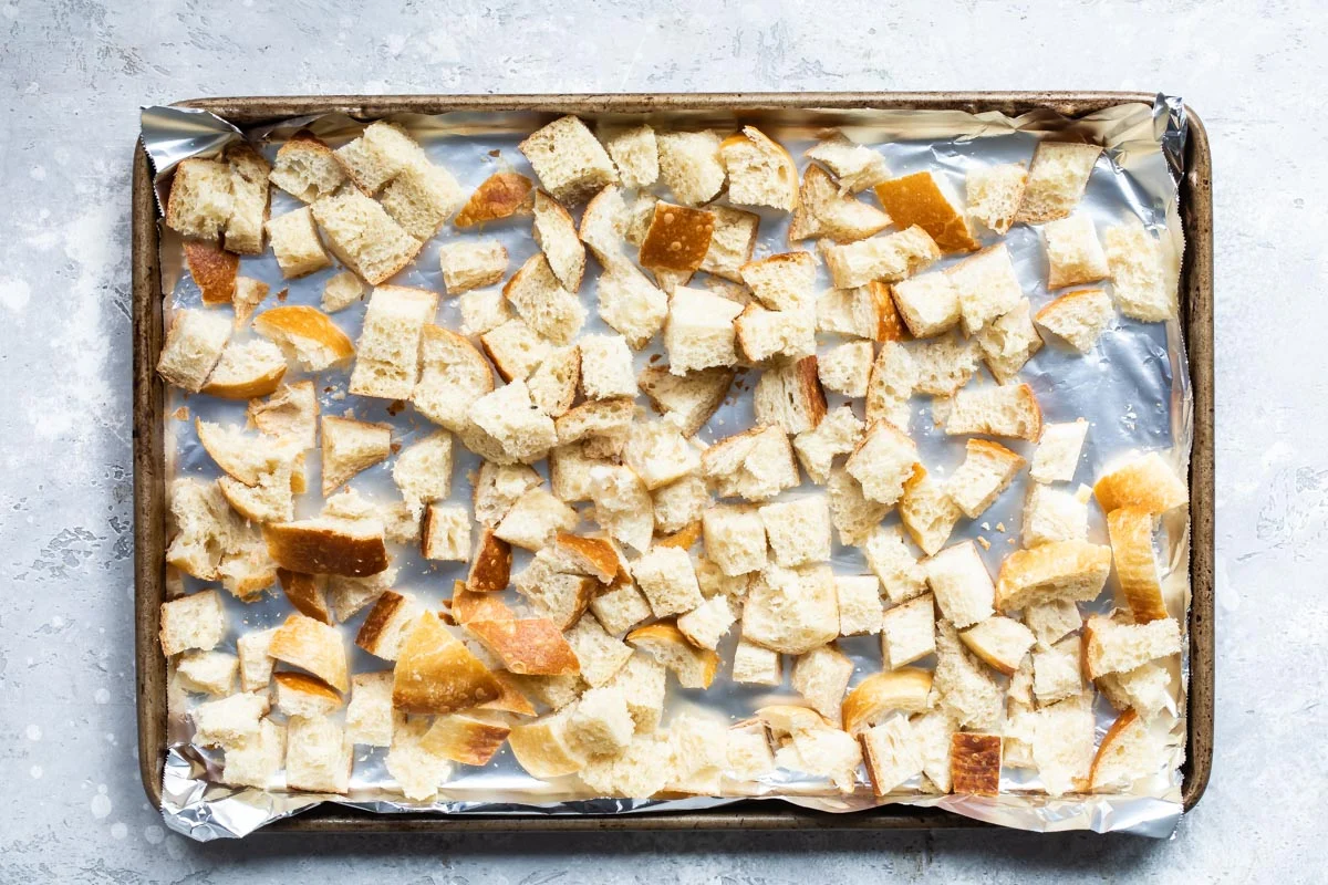A sheet pan covered with dried bread cubes in a home oven with warm kitchen lighting