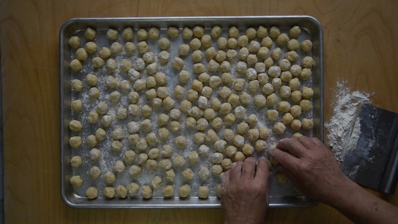 A sheet pan filled with small raw struffoli dough balls dusted lightly with flour, ready for frying