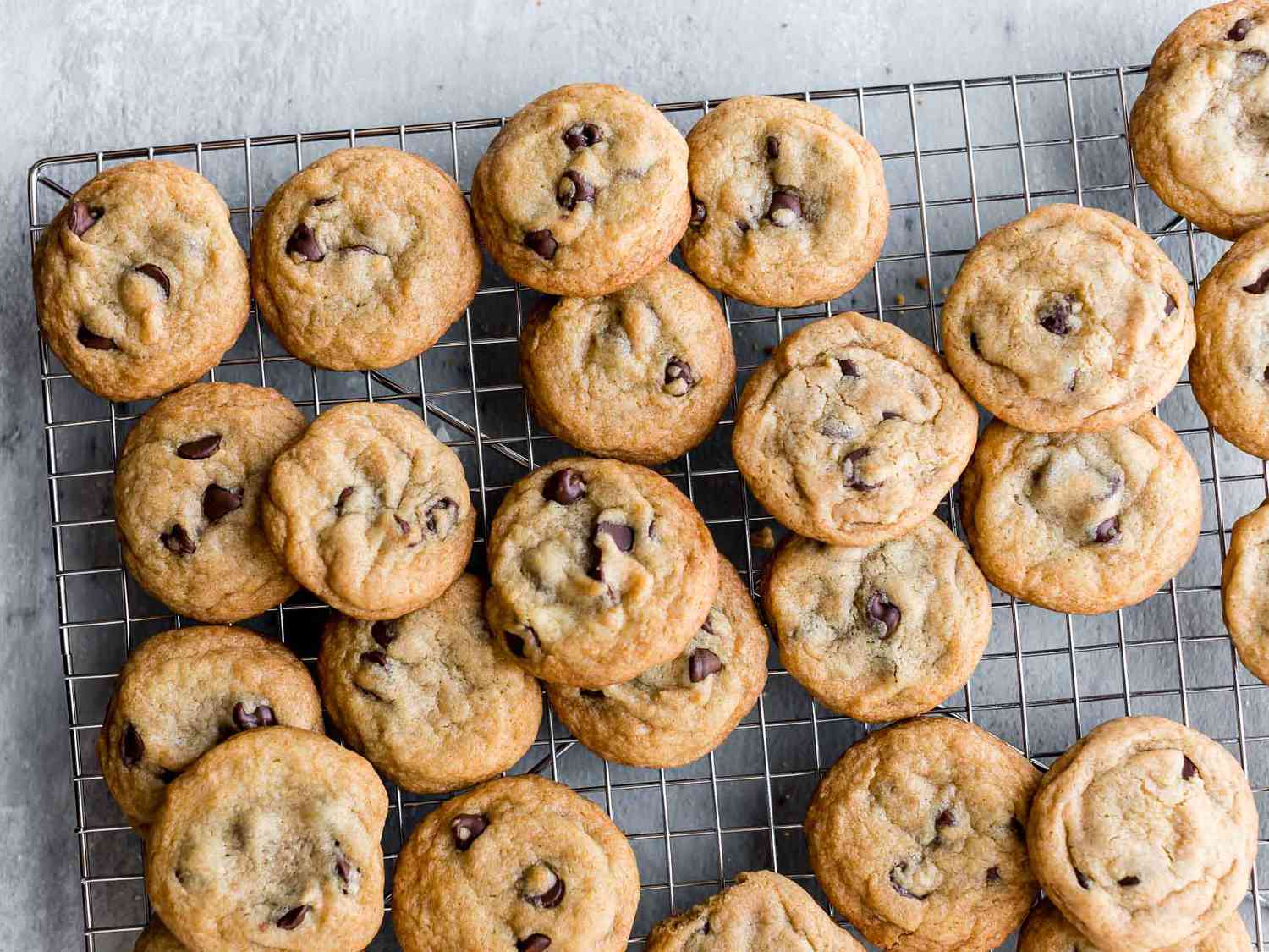 A sheet pan of chocolate chip cookie dough portions baking in an oven with edges just beginning to turn golden