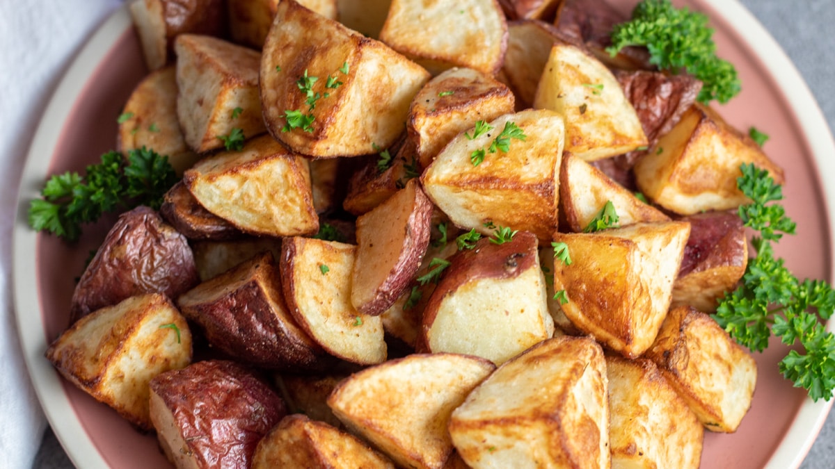 A sheet pan of crispy baked red potato wedges with browned edges, garlic and herbs, on parchment paper in a warm home kitchen