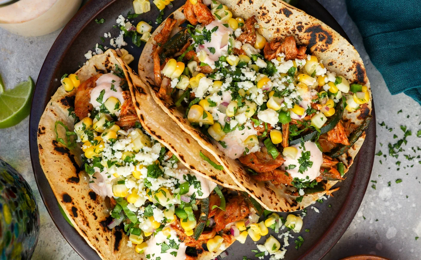 A sheet pan of crispy chicken tacos with melted cheese, browned tortilla edges, and fresh cilantro on a kitchen counter under warm light