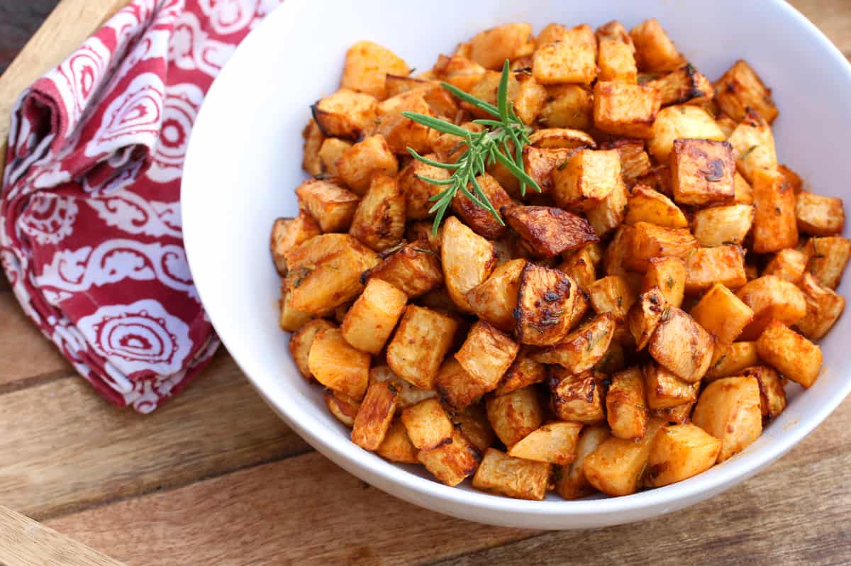 A sheet pan of golden brown honey roasted rutabaga cubes with crispy edges, scattered thyme leaves, and a lemon half on the side on a warm kitchen counter