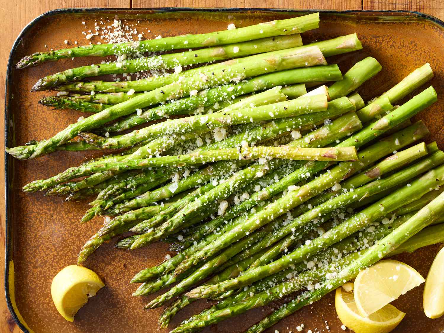 A sheet pan of roasted asparagus spears with crisp tips and a light sprinkle of Parmesan on a warm kitchen counter