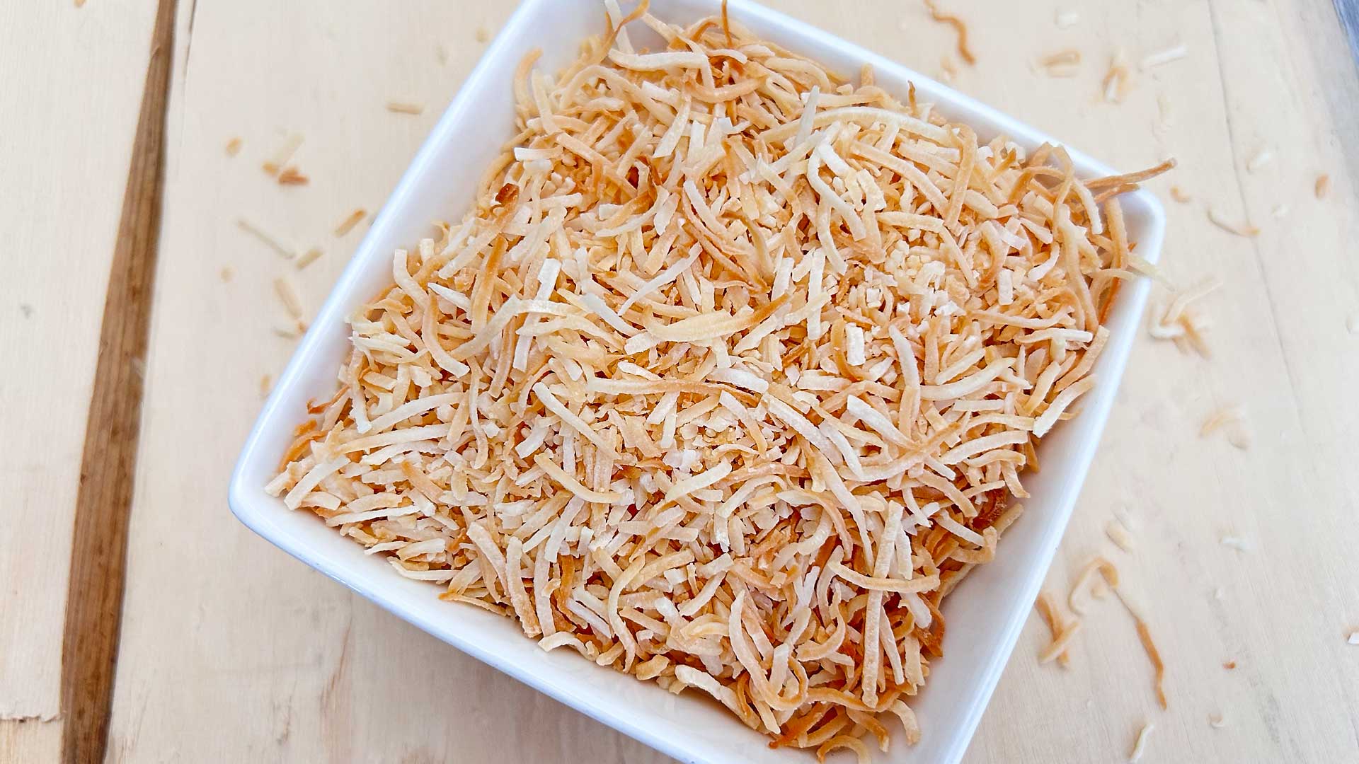 A sheet pan of shredded coconut turning lightly golden in a home oven, with warm kitchen lighting
