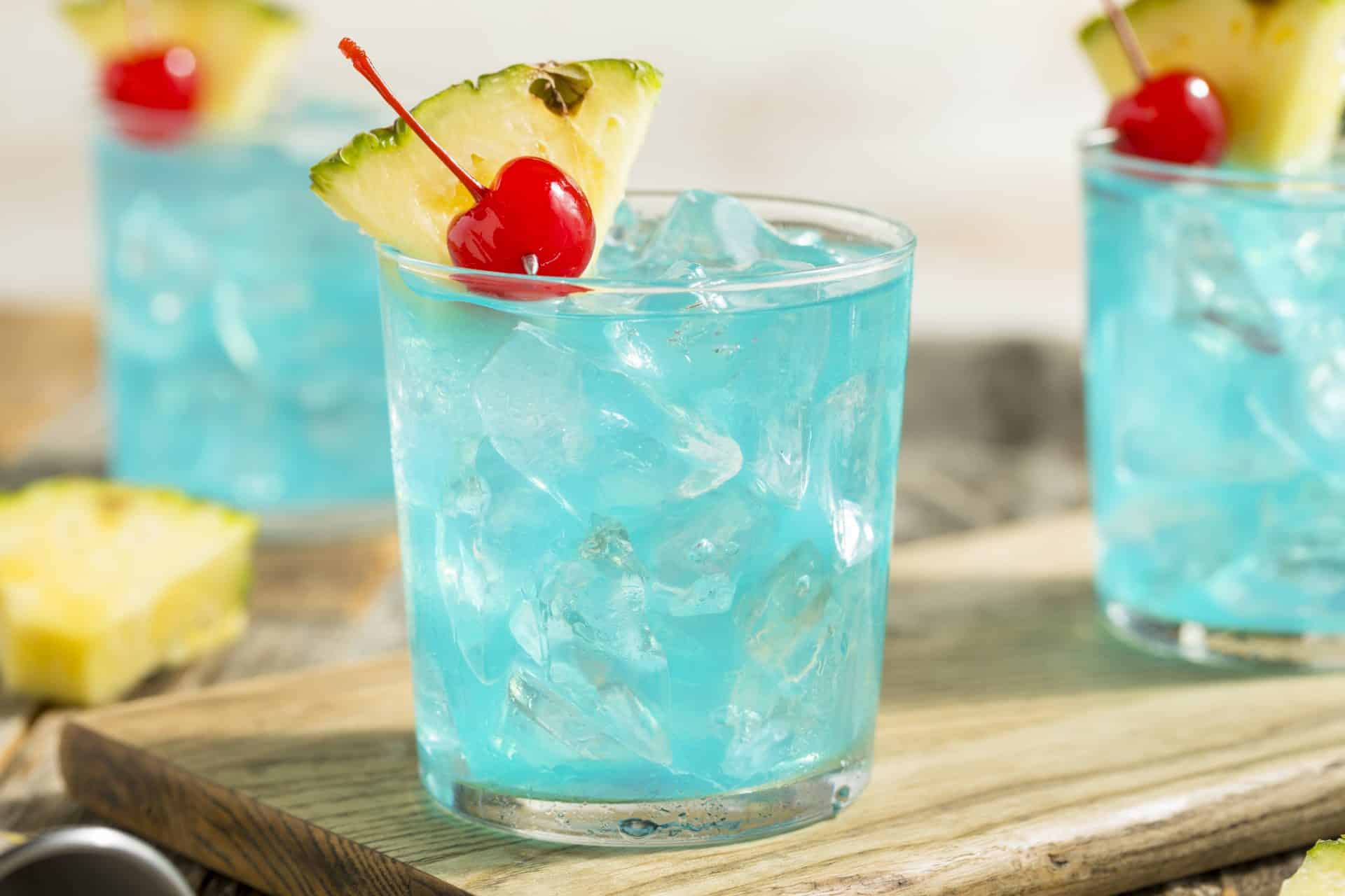 A single Blue Hawaiian cocktail in a hurricane glass with crushed ice, a pineapple wedge, and a maraschino cherry on a bright kitchen counter