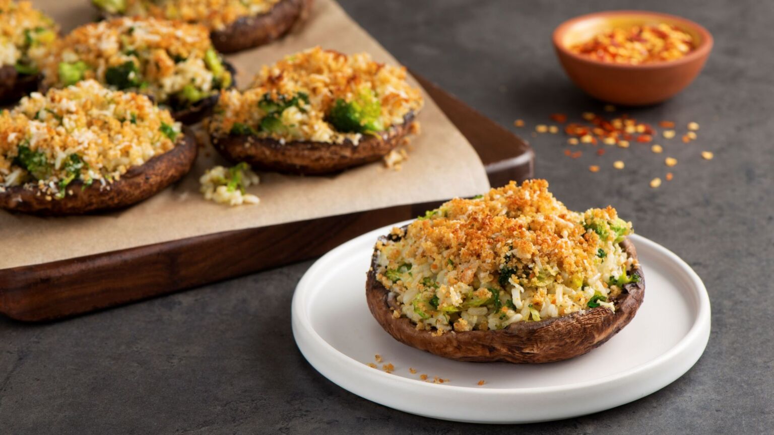 A single baked portobello mushroom cap stuffed with creamy spinach and cheese, topped with golden breadcrumbs, on a white plate with a fork on a warm-toned kitchen table
