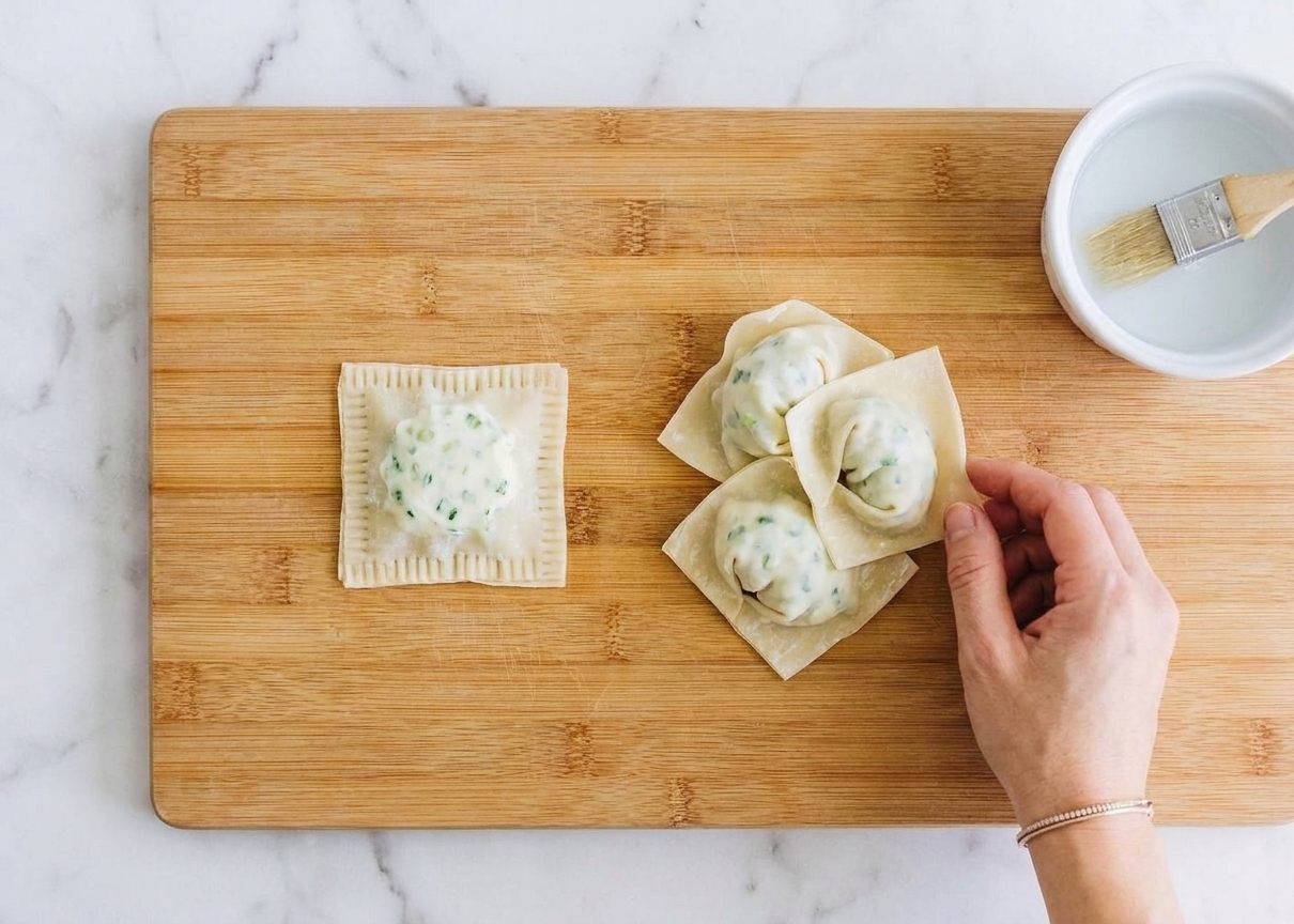 A single folded wonton with sealed edges sitting on a wooden board, with several finished wontons nearby
