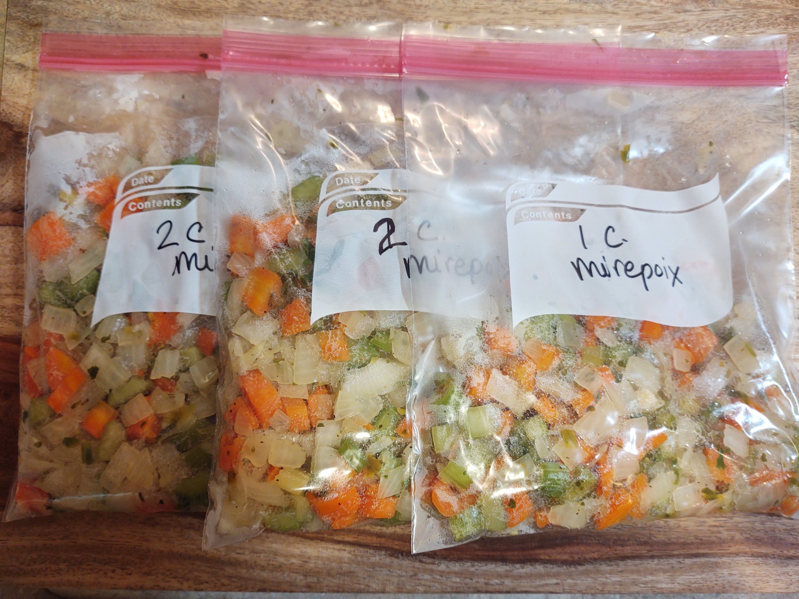 A single freezer bag laid flat on a countertop filled with chopped onion, carrot, and celery, ready to be labeled and frozen