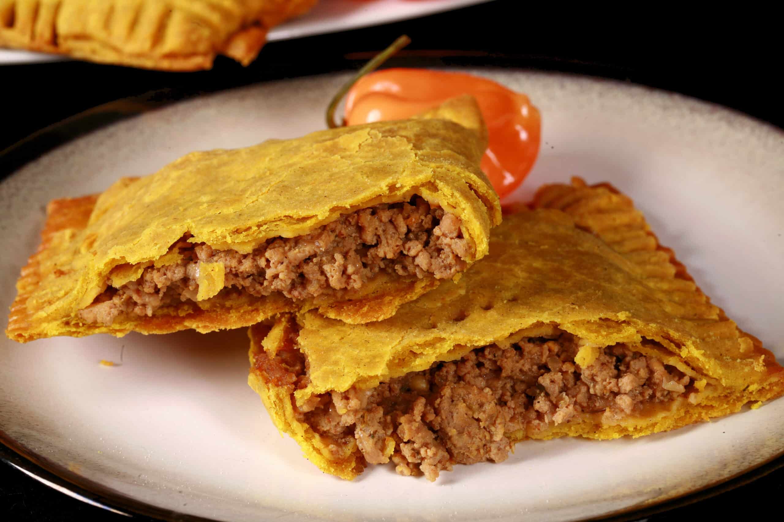 A single golden Jamaican beef patty split open on a ceramic plate, showing the juicy spiced beef filling, with a simple napkin and fork on a warm wooden table