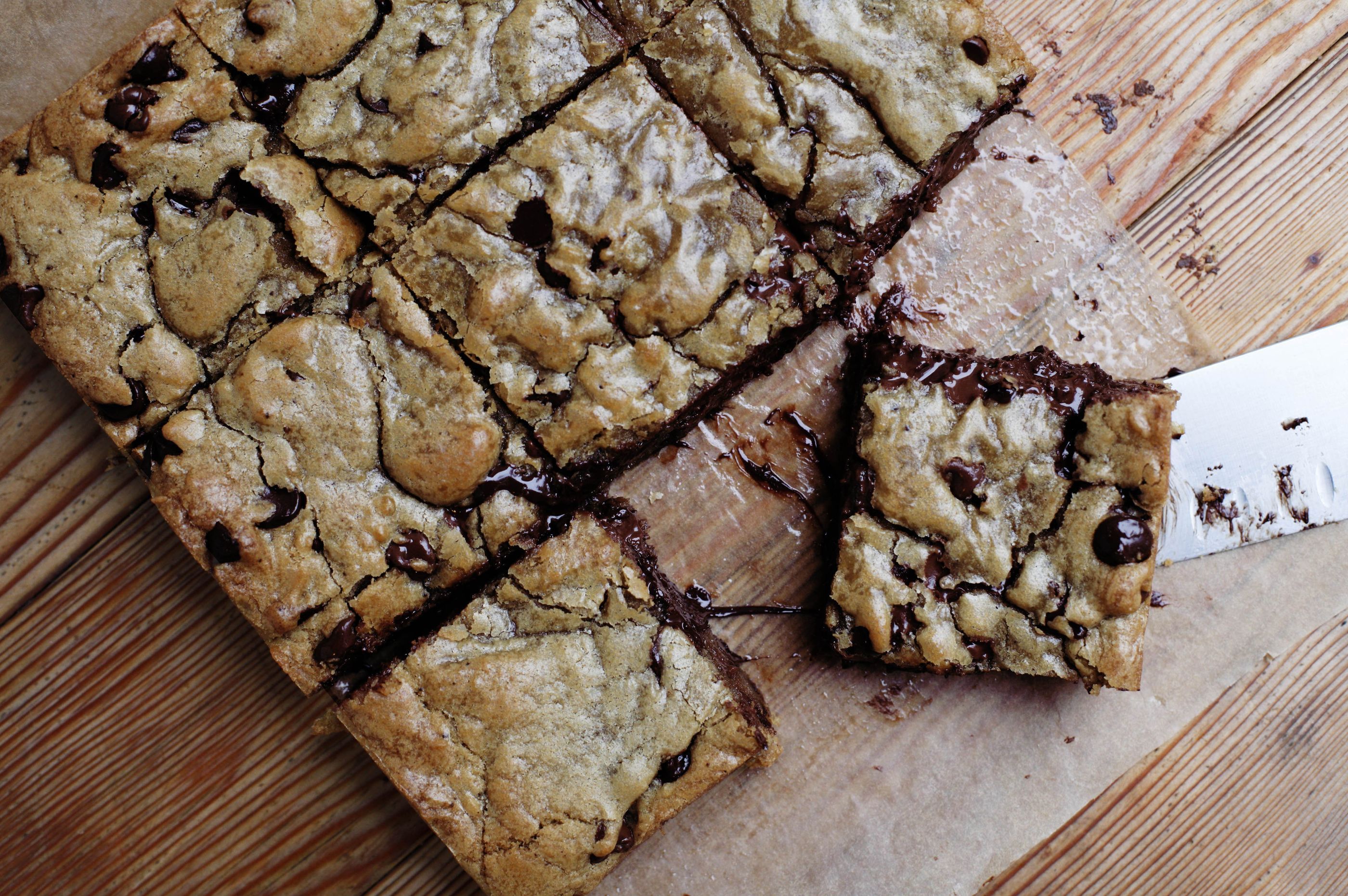 A single pan of golden brown butter blondies with crackly tops and flaky sea salt sprinkled over the surface, photographed on a warm kitchen counter under soft natural light
