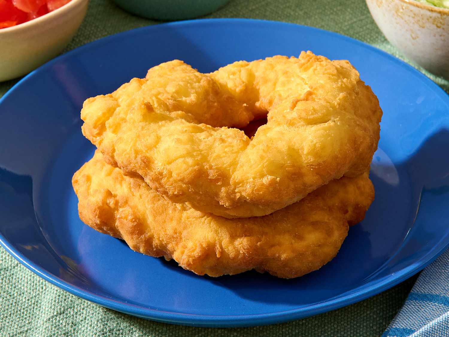 A single piece of Navajo fry bread, golden and blistered with crisp edges, served on a simple ceramic plate on a warm-toned kitchen table