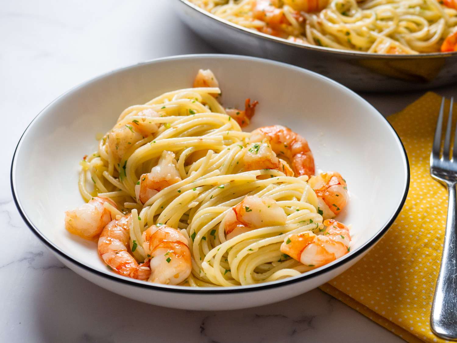 A single plate of shrimp scampi over linguine with glossy garlic butter sauce, lemon wedges, and chopped parsley on a warm kitchen table