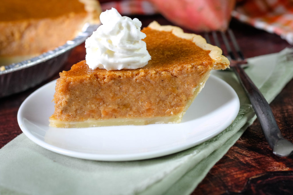 A single slice of Southern sweet potato pie on a dessert plate with a fork beside it, warm kitchen lighting, flaky crust visible