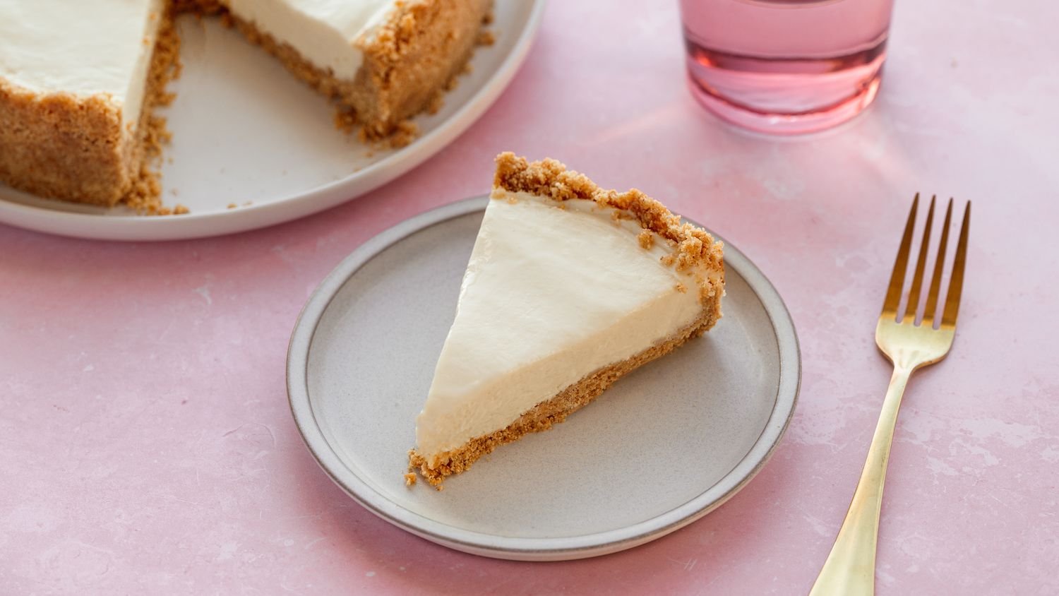 A single slice of creamy no-bake cheesecake on a small plate with a graham cracker crust and a glossy berry topping on a neutral-toned kitchen table