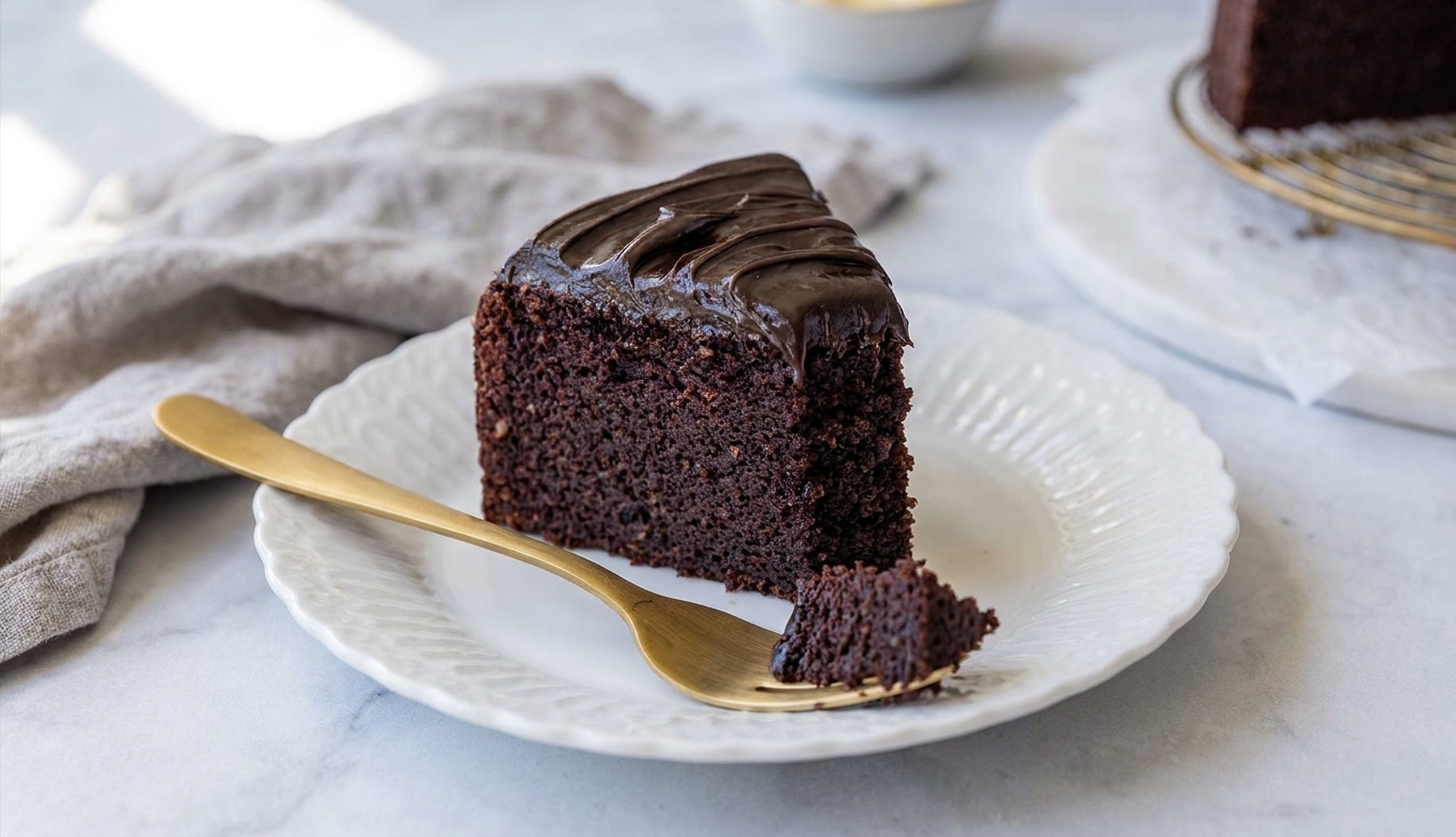 A single slice of moist gluten-free chocolate cake on a small plate with a fork, showing a tender crumb and thick chocolate frosting