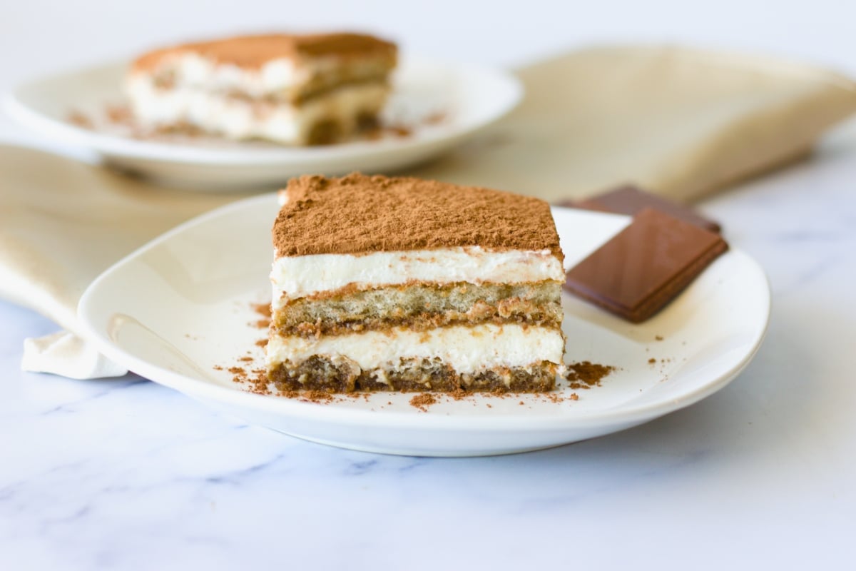 A single slice of tiramisu on a small plate with visible layers of mascarpone cream and espresso-soaked ladyfingers