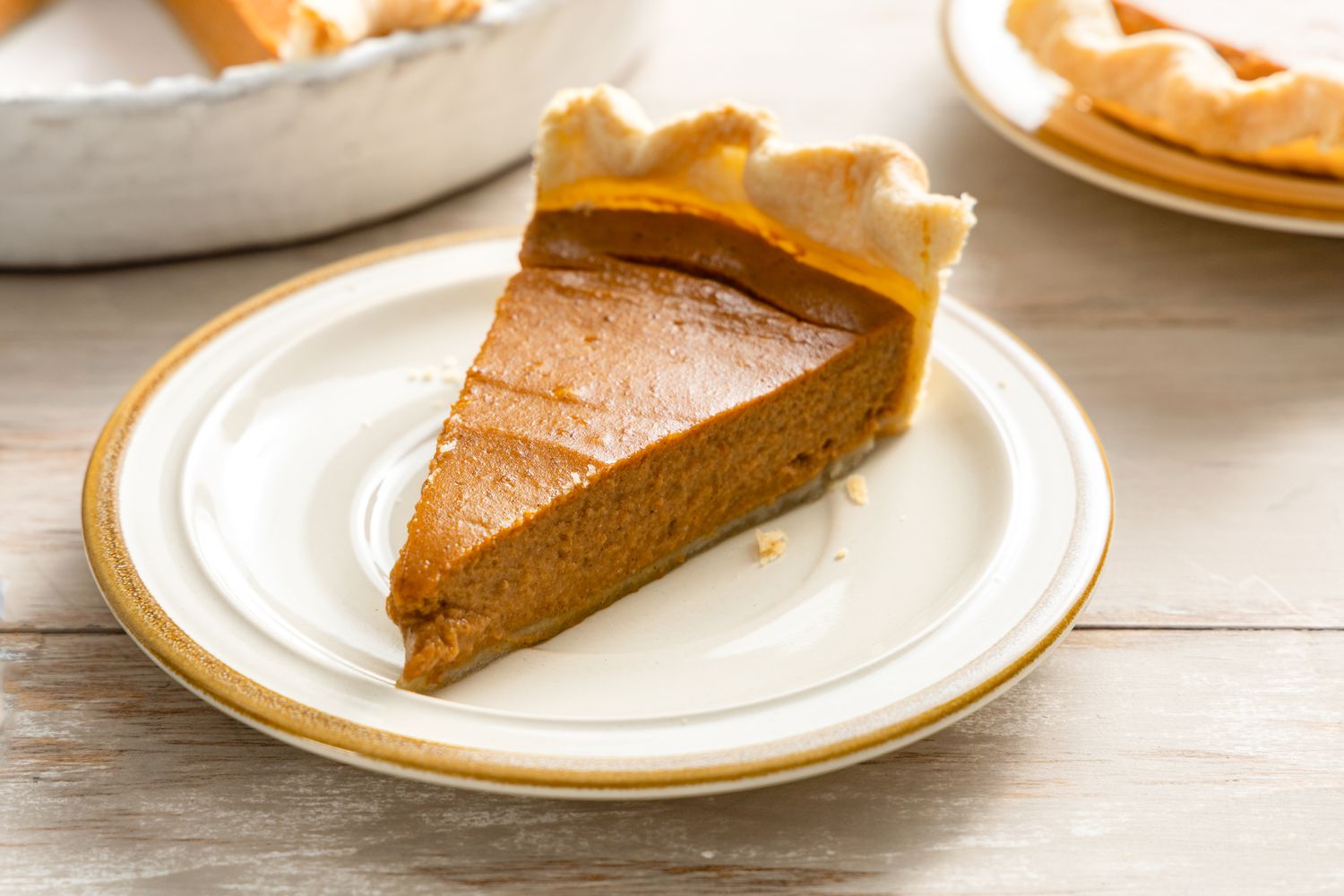 A single slice of vegan pumpkin pie on a dessert plate with a dollop of coconut whipped cream, photographed on a warm-toned kitchen table with soft natural light
